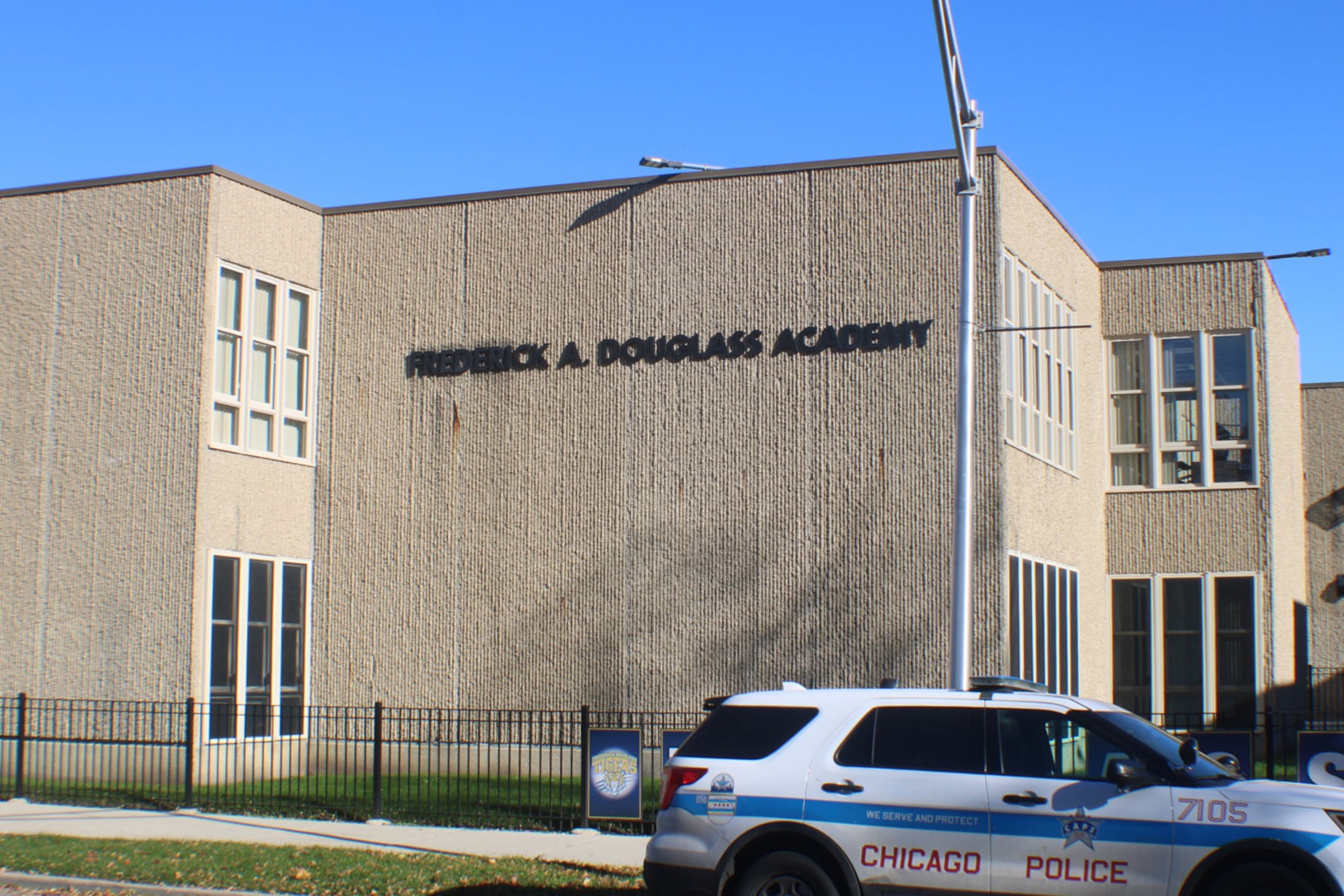 The side of a tan brick school with the name of the school on the side of the building with a Chicago Police car in the foreground.
