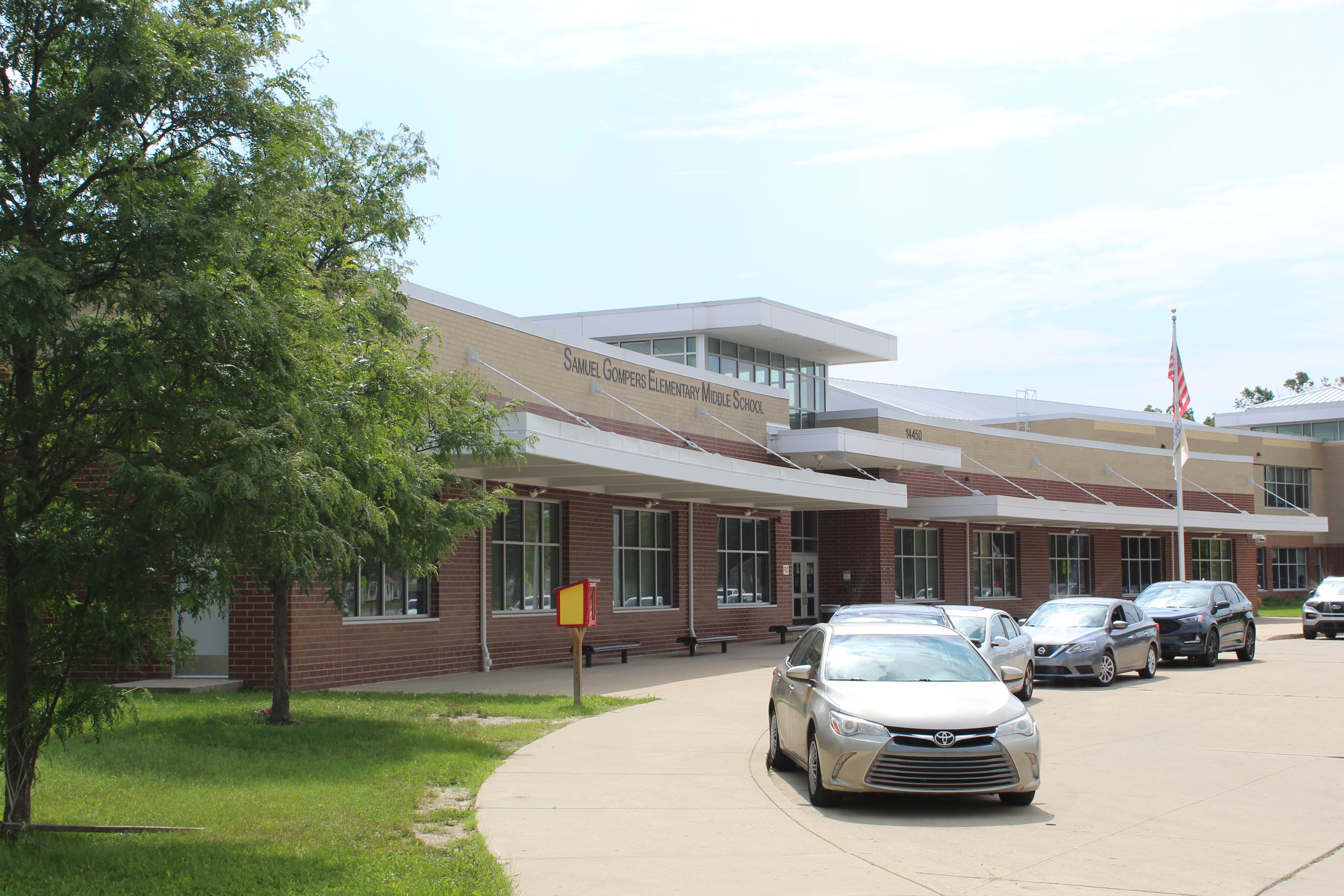 A row of cars are parked in front of a school building.