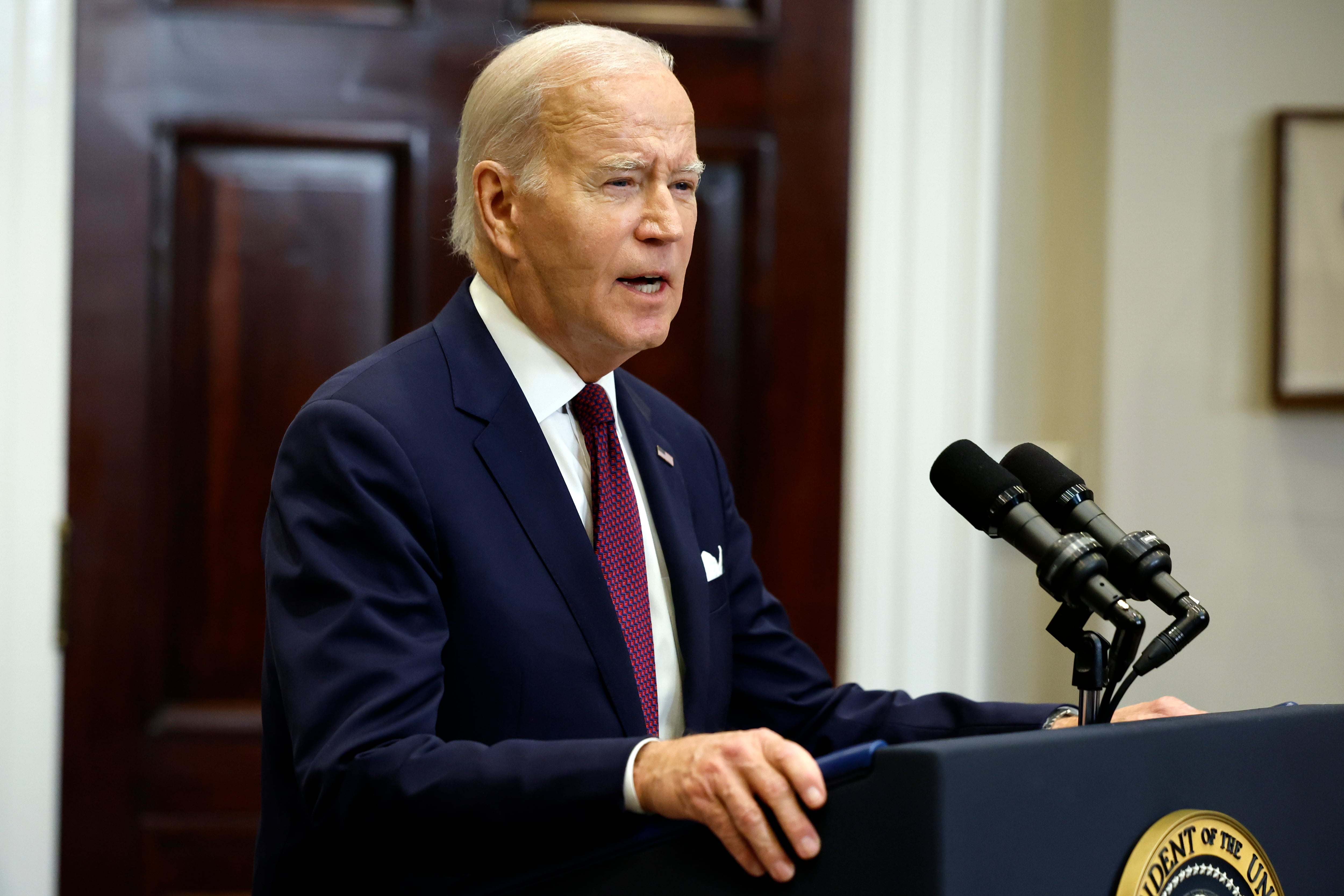 U.S. President Joe Biden speaks into a microphone while wearing a suit in the White House.