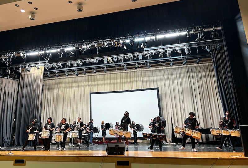 A photograph of a group of students in a drum line on a stage.