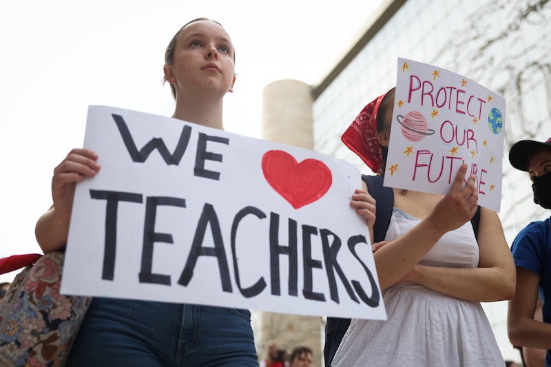 Protesters hold signs in front of an official-looking building.