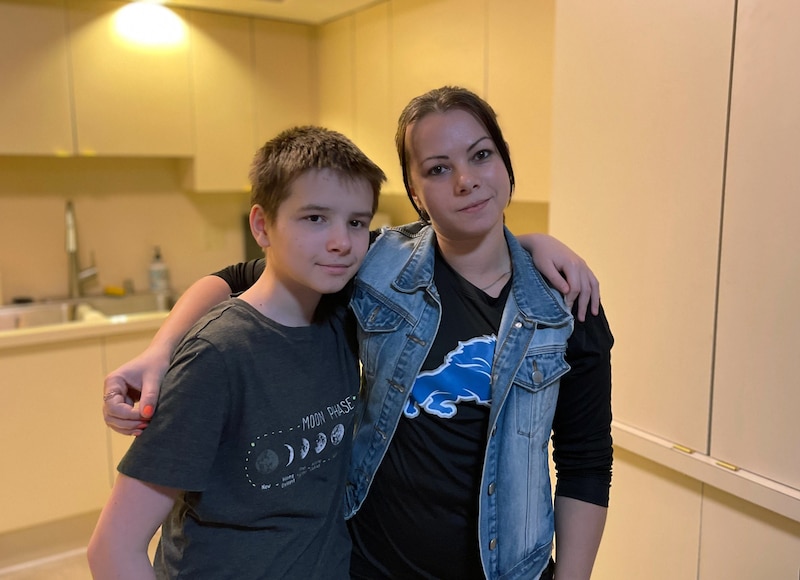 A young boy stands next to his mother posing for a photograph in their kitchen.