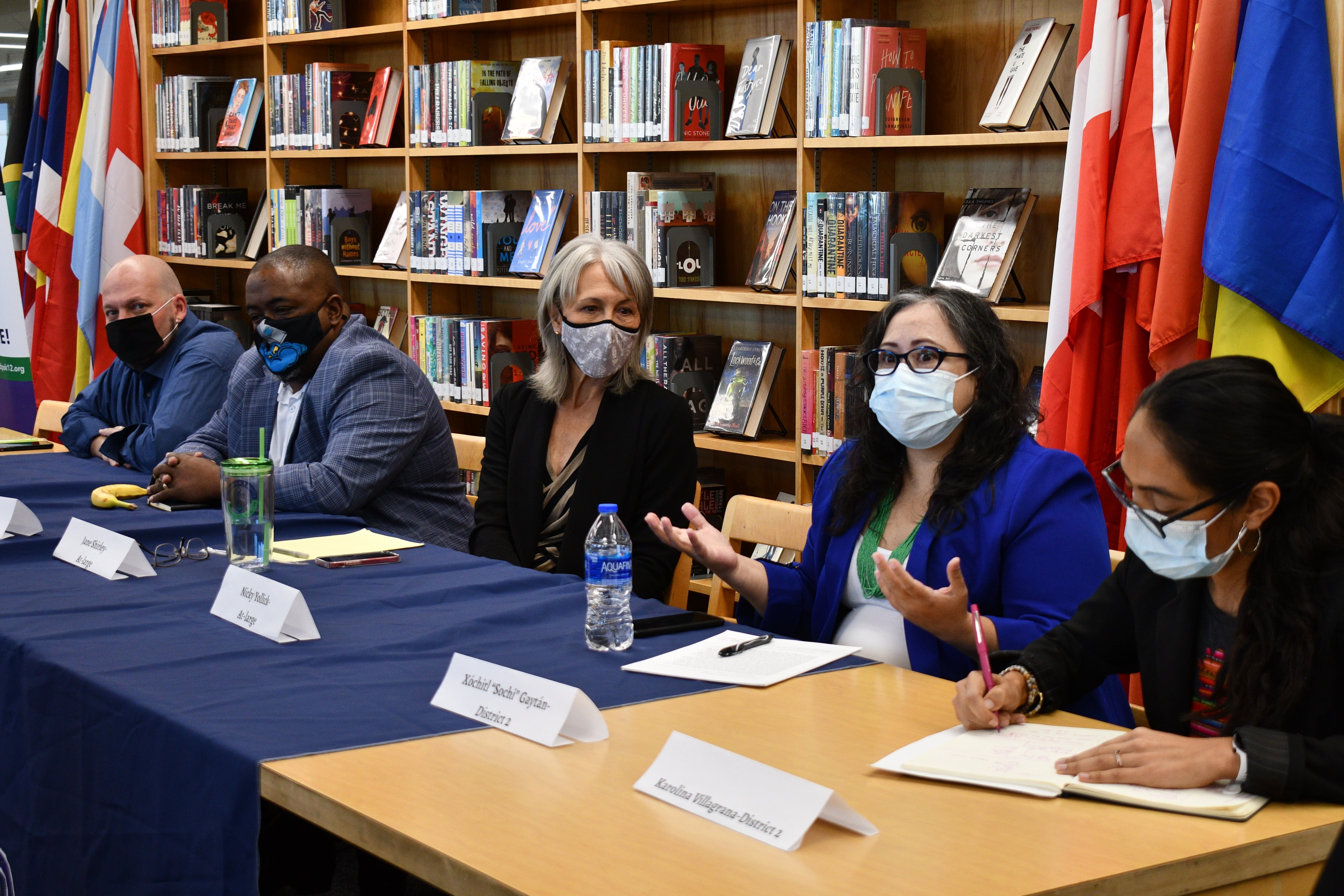 Five Denver school board candidates sit at a table in a high school library during a candidate forum. The candidates are wearing masks.