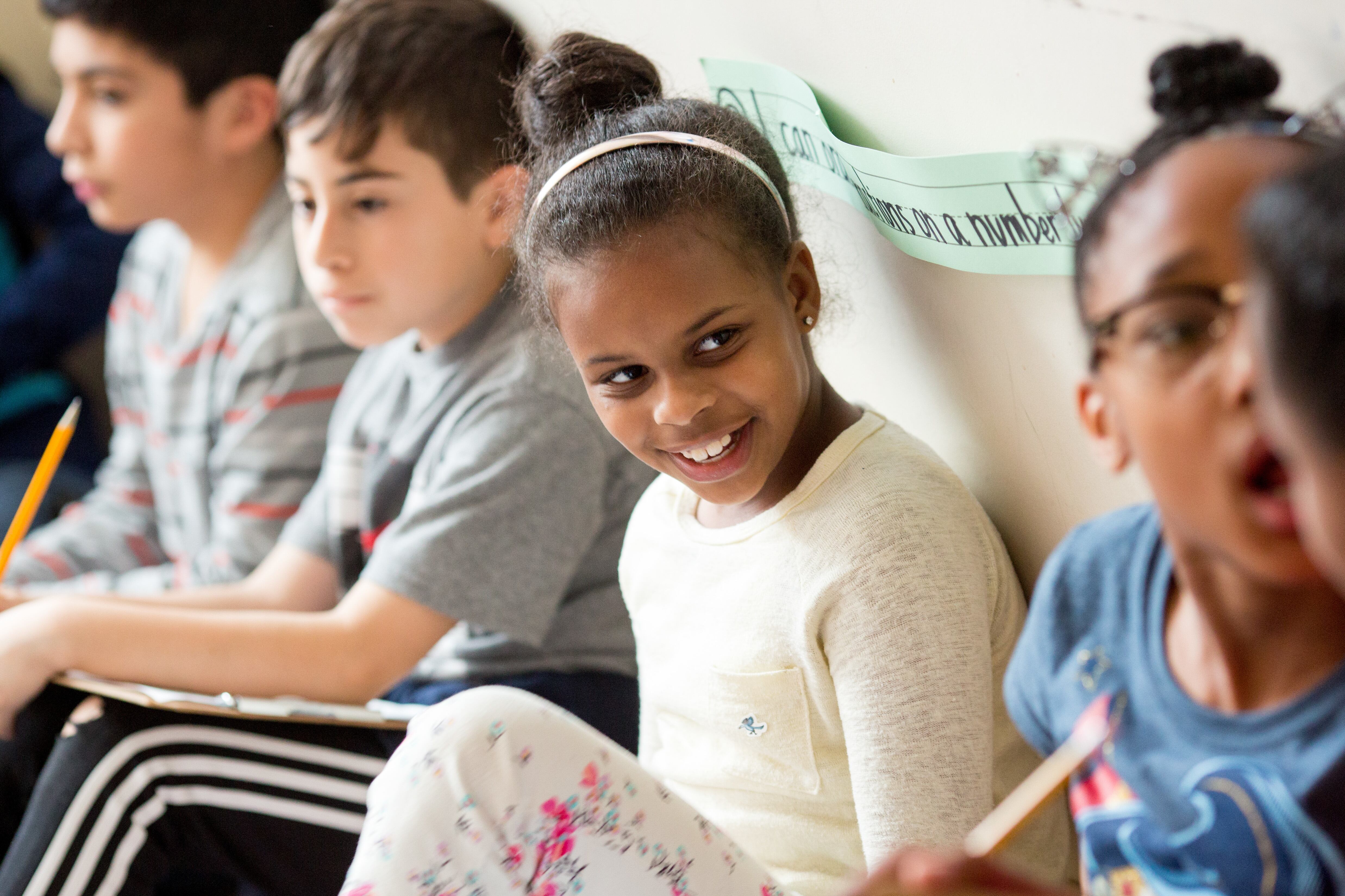 Students sit against a wall in a class.
