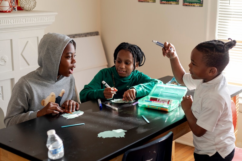 Three young children work at a table inside a house.
