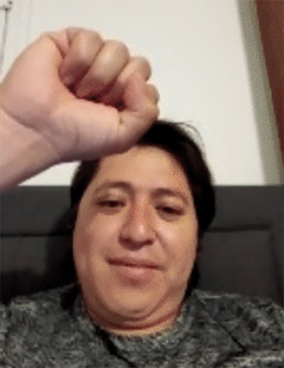A screenshot of a person on a zoom call with dark hair holding their fist in the air.