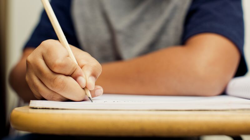 Student holds a pencil to a notebook placed on a desk.