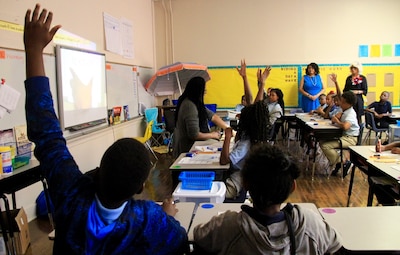 Students and adults sit at desks in a classroom.