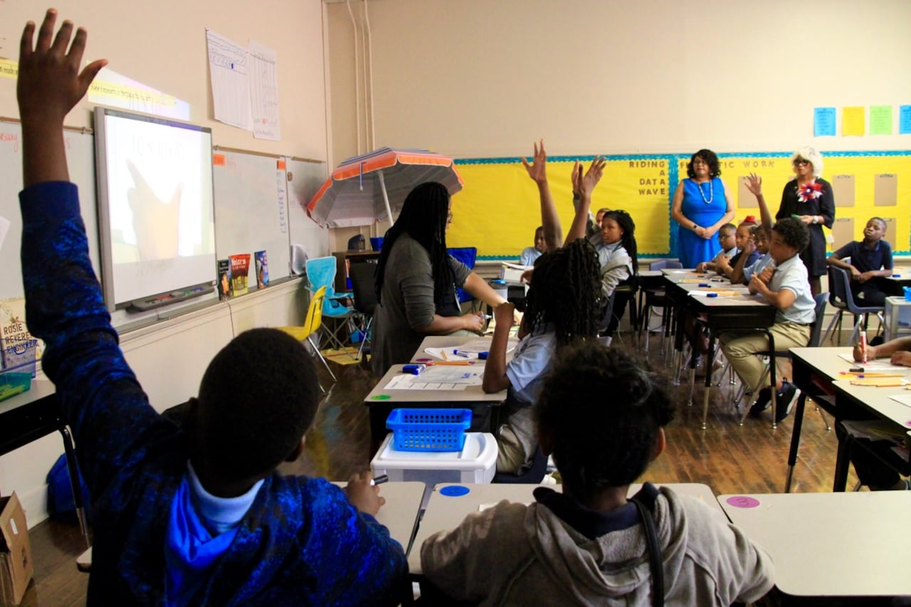 Students and adults sit at desks in a classroom.