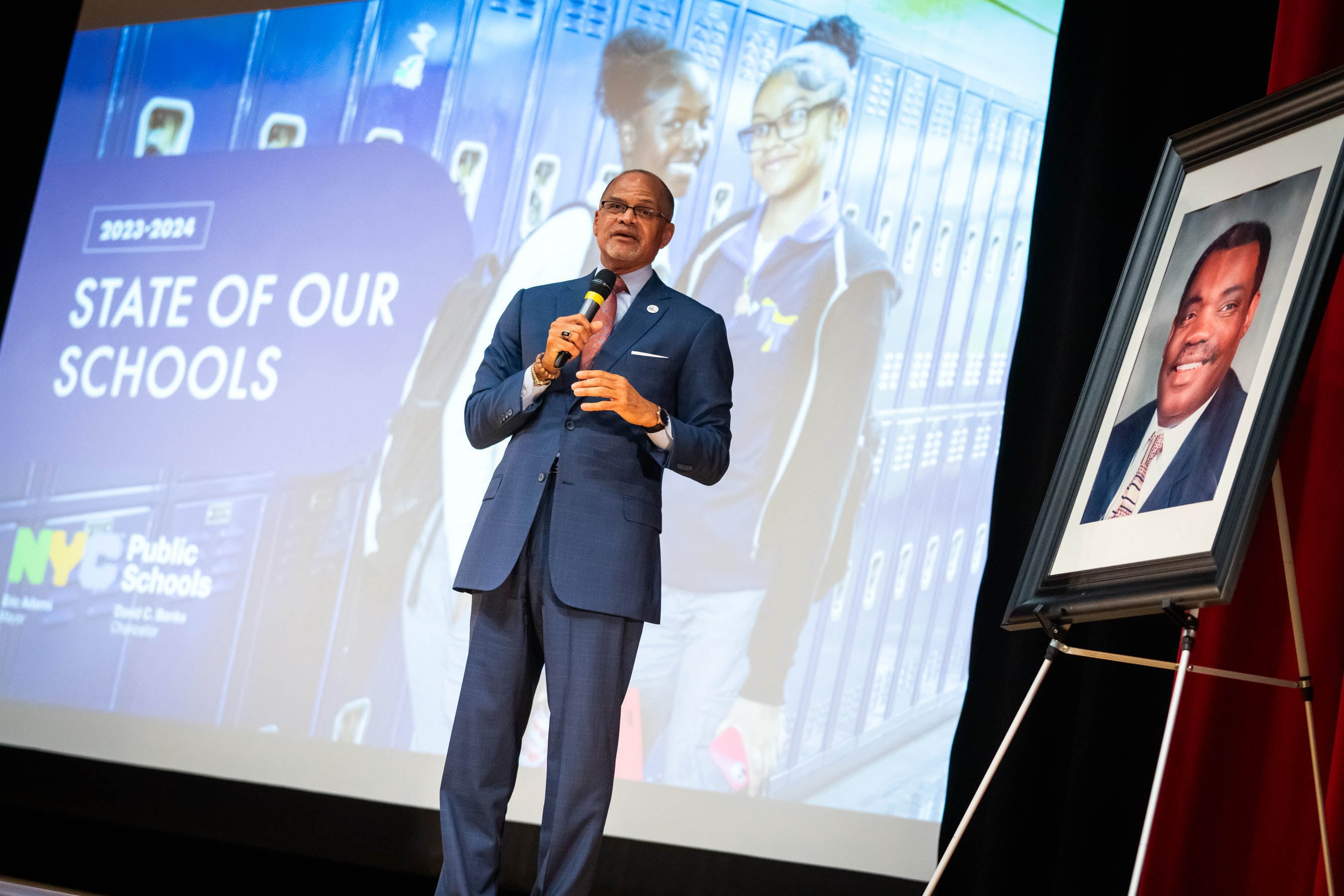 A man in a blue suit stands in front of a projected screen.