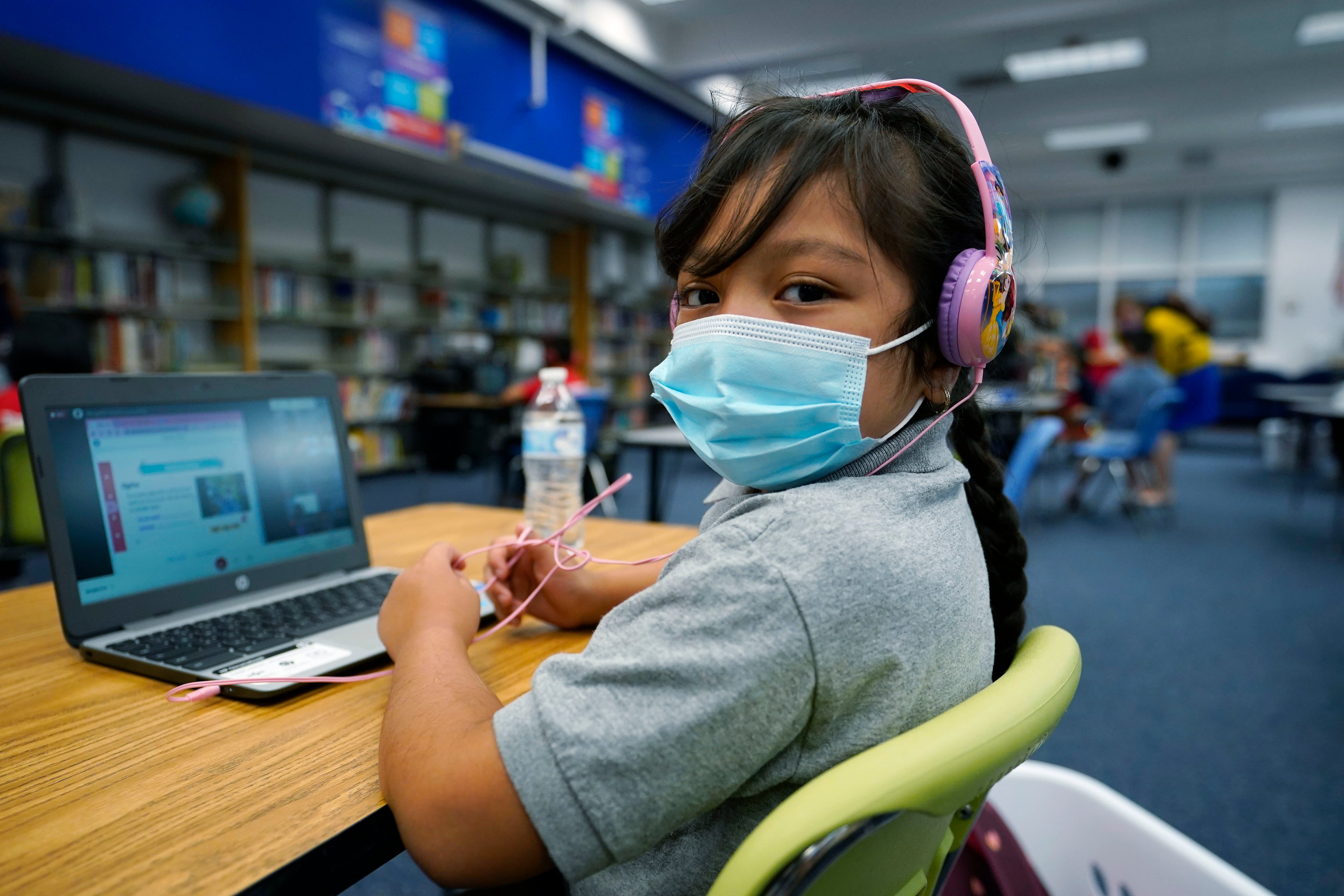 Masked girl works on her laptop at a learning center.
