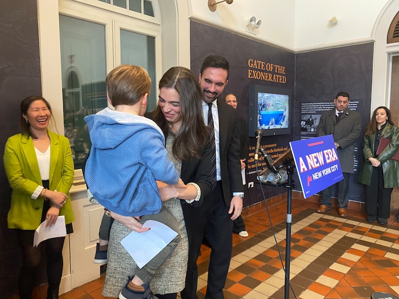 A woman picks up a young boy as a man in a suit smiles.