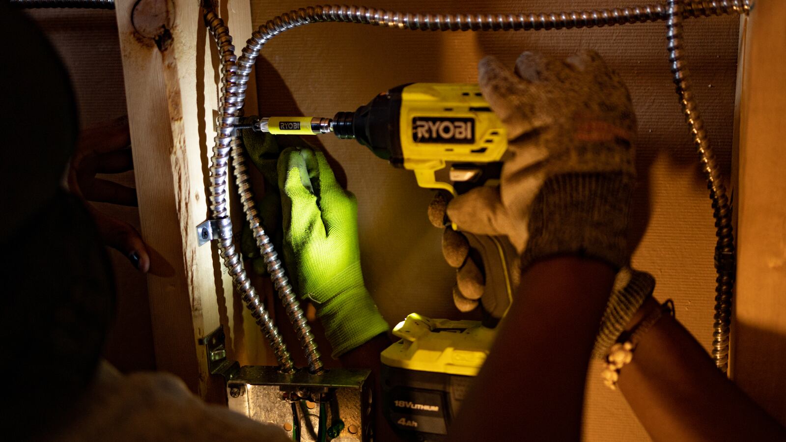 Students work on the electrical inside of a shed, using a Ryobi power drill.