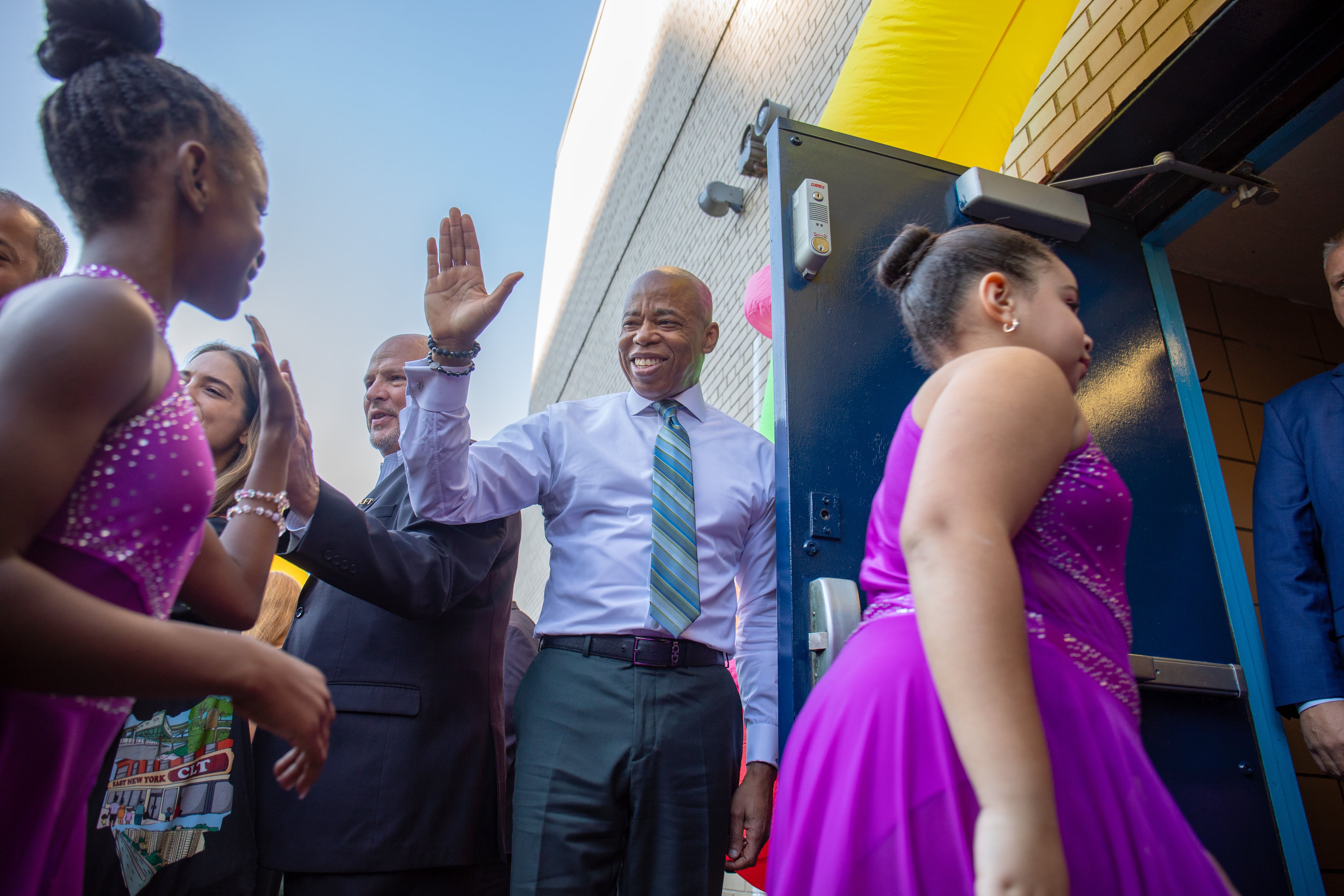 A photograph of NYC mayor, Eric Adams, reaching out for a high five while a line of young students walk by.