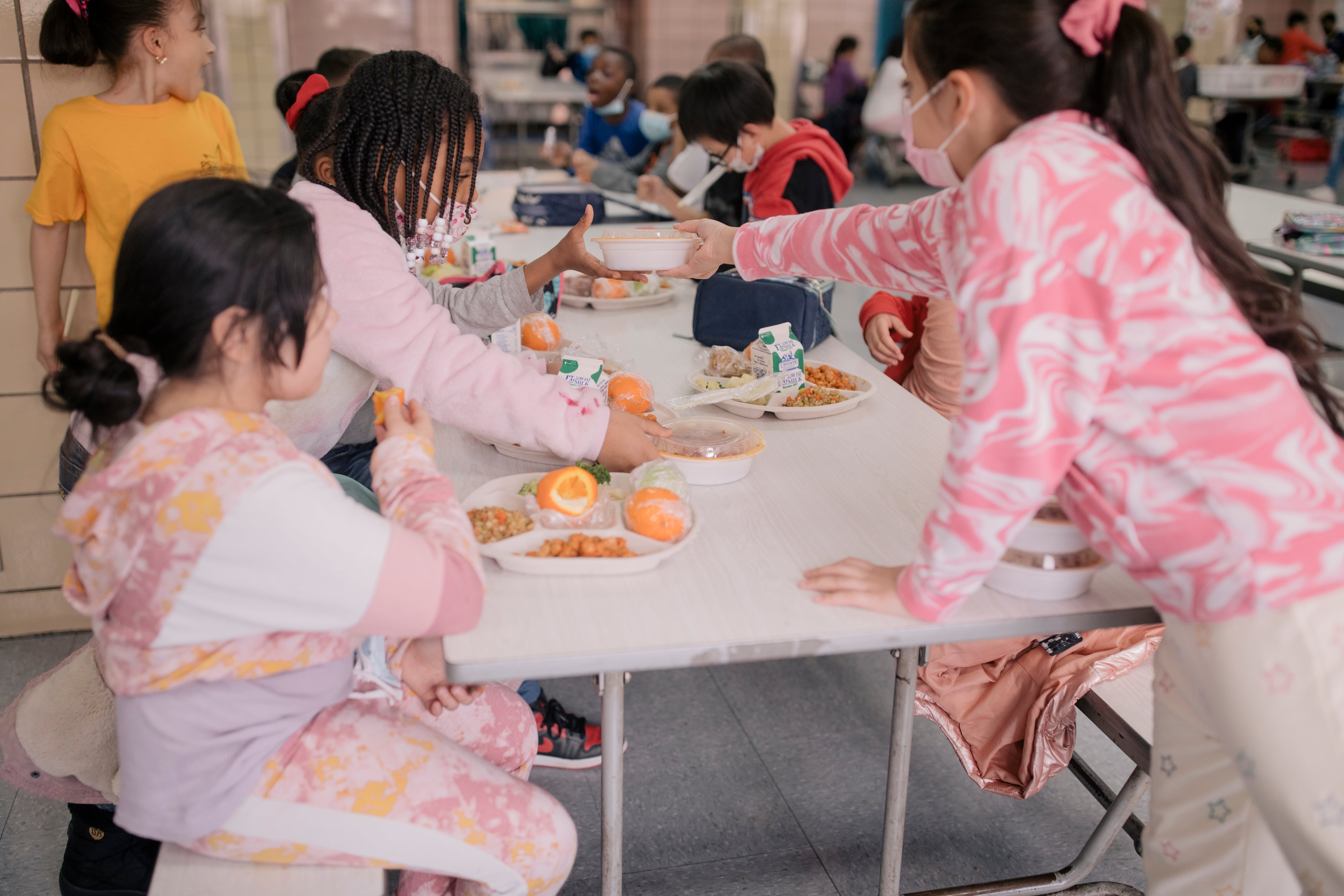A group of girls, all wearing pink, eat together in a school cafeteria.
