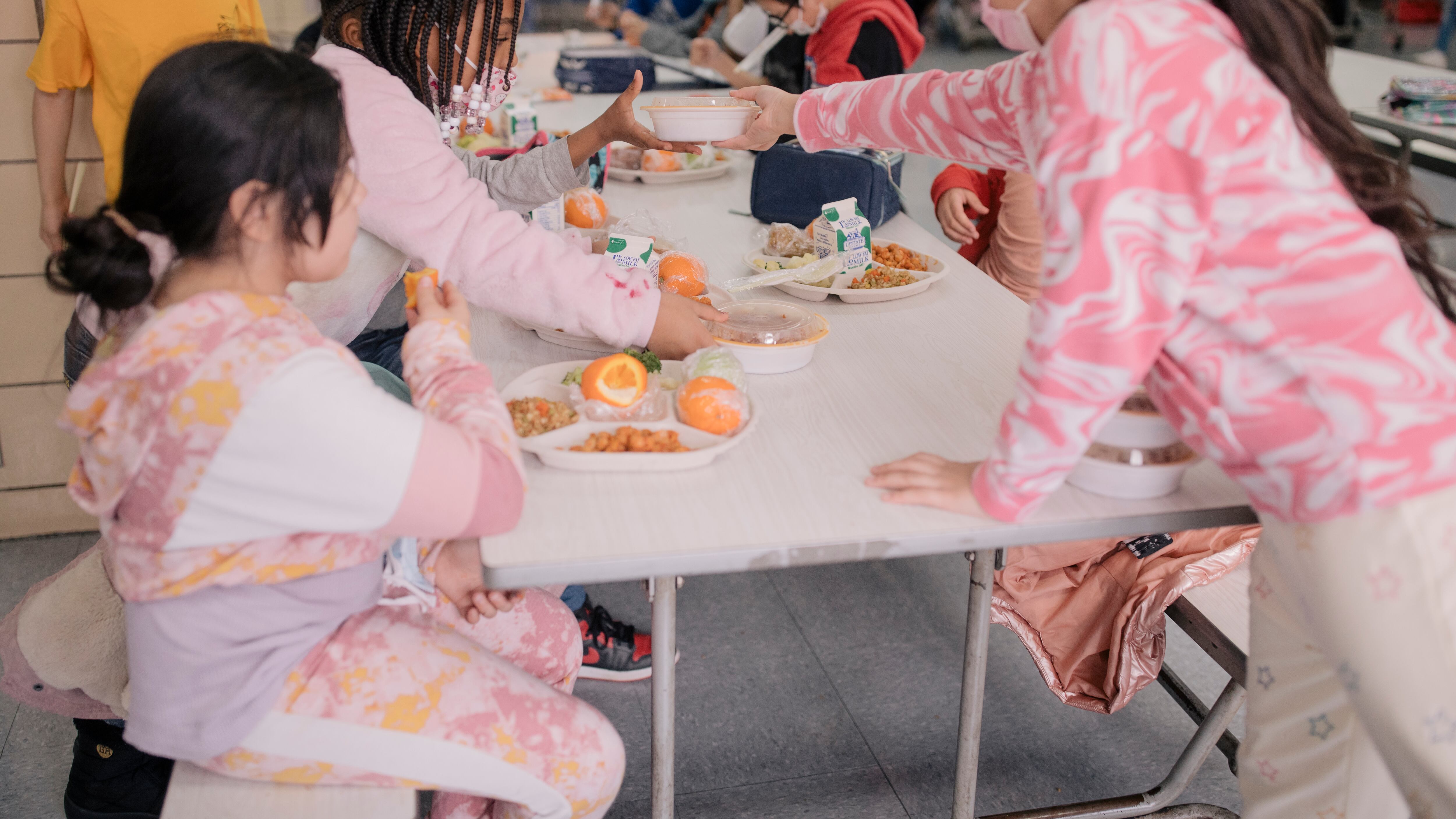 A group of girls, all wearing pink, eat together in a school cafeteria.