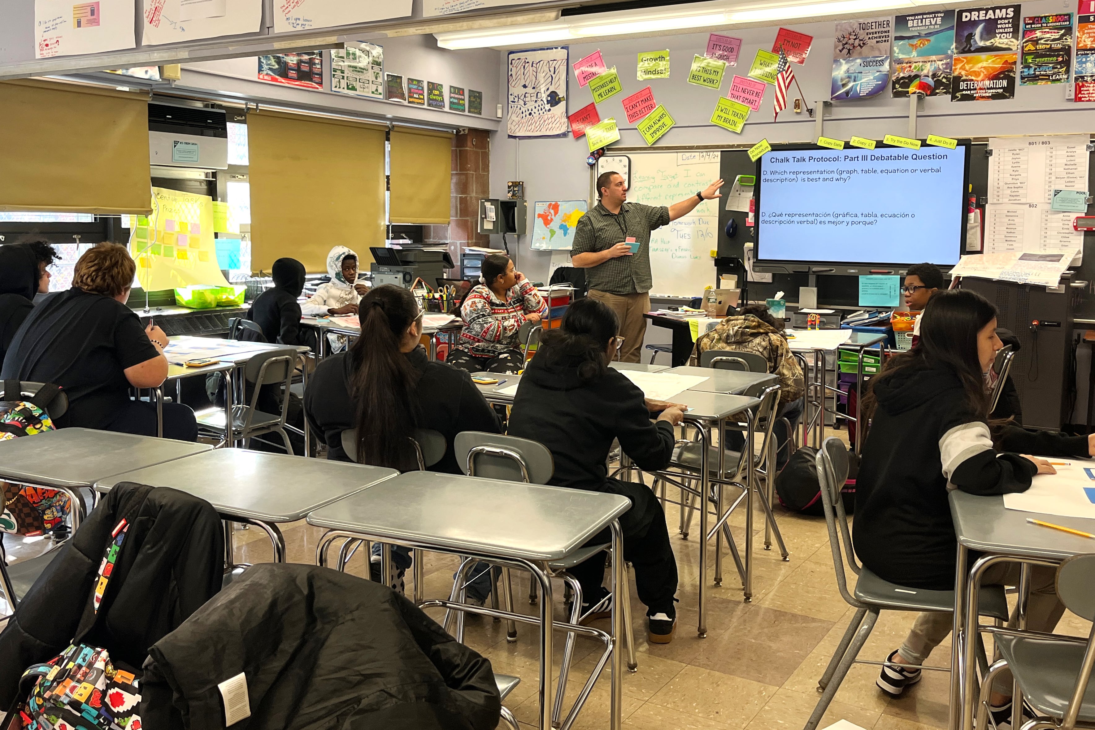 A man points to a screen in front of a classroom of students