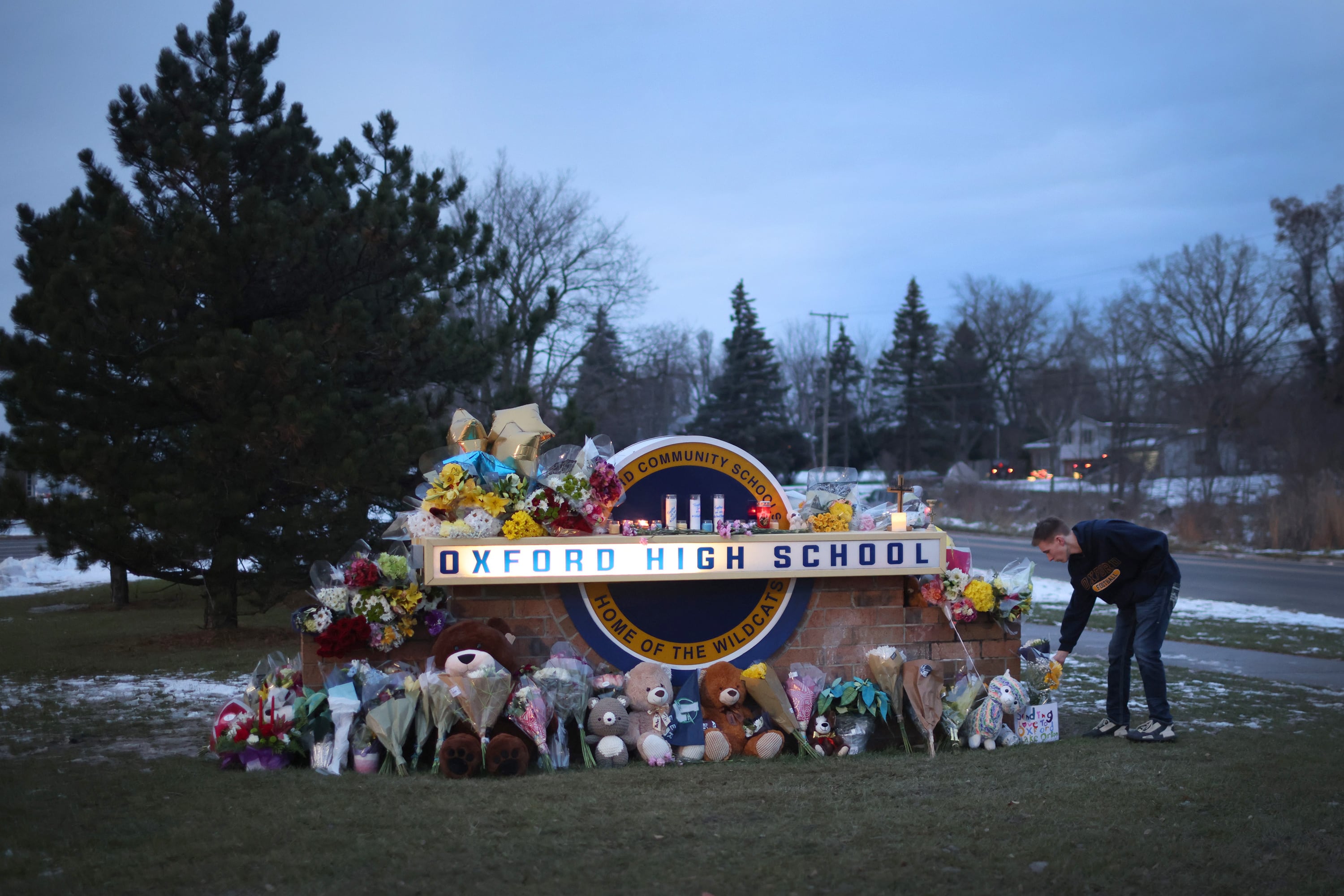 A person places a flower down on a memorial for the Oxford High School victims near a road outside of the school.