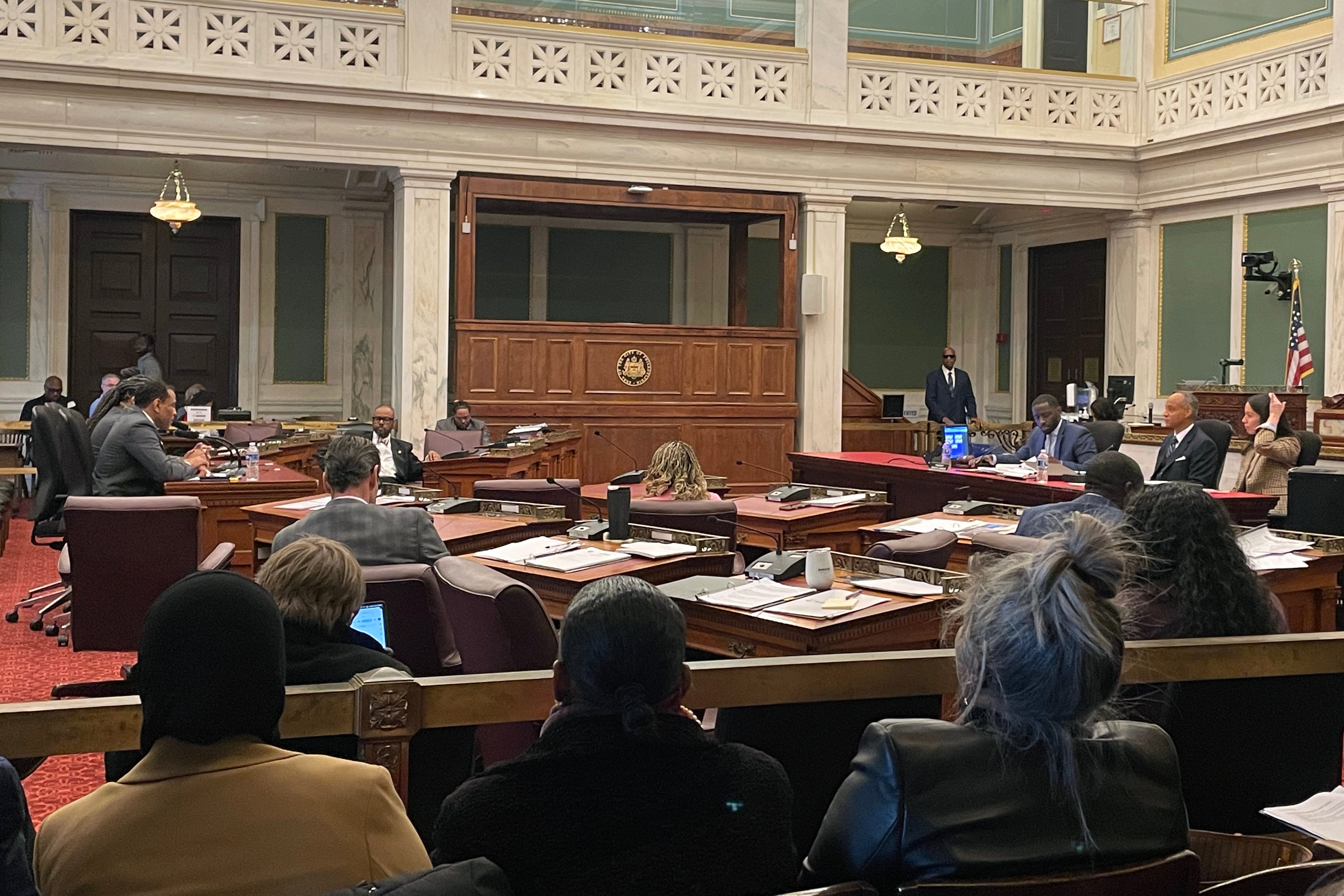 A photograph of a large meeting room with people sitting at tables and chairs around the whole room.