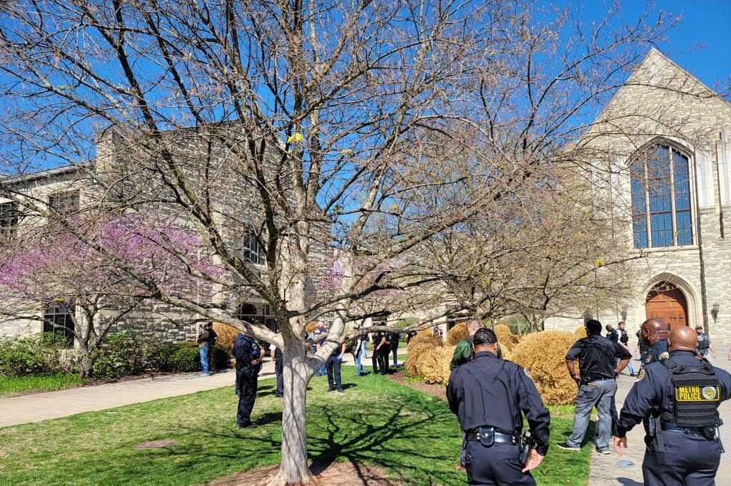 Police officers in uniform outside a school building, next to a tree.