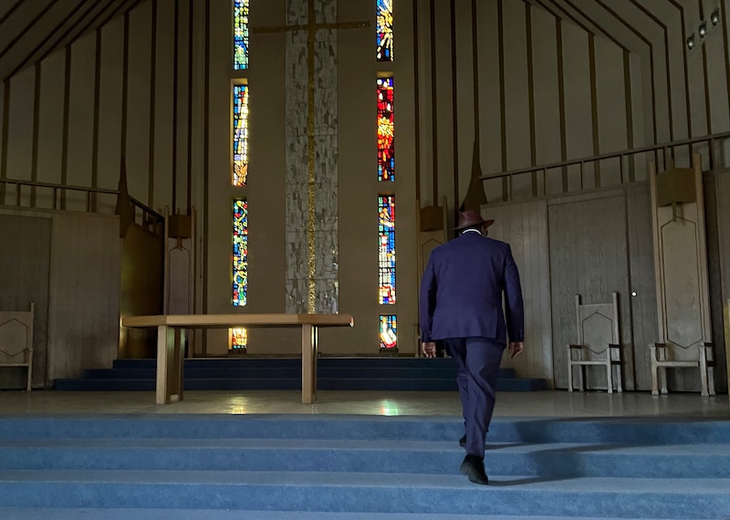 A man in a suit walks up stairs inside of a chapel.