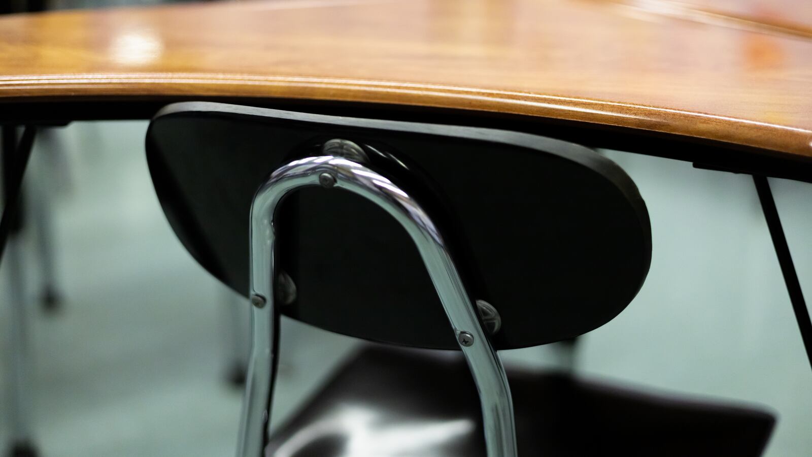 In a classroom sits an empty blue chair next to a wooden desk.