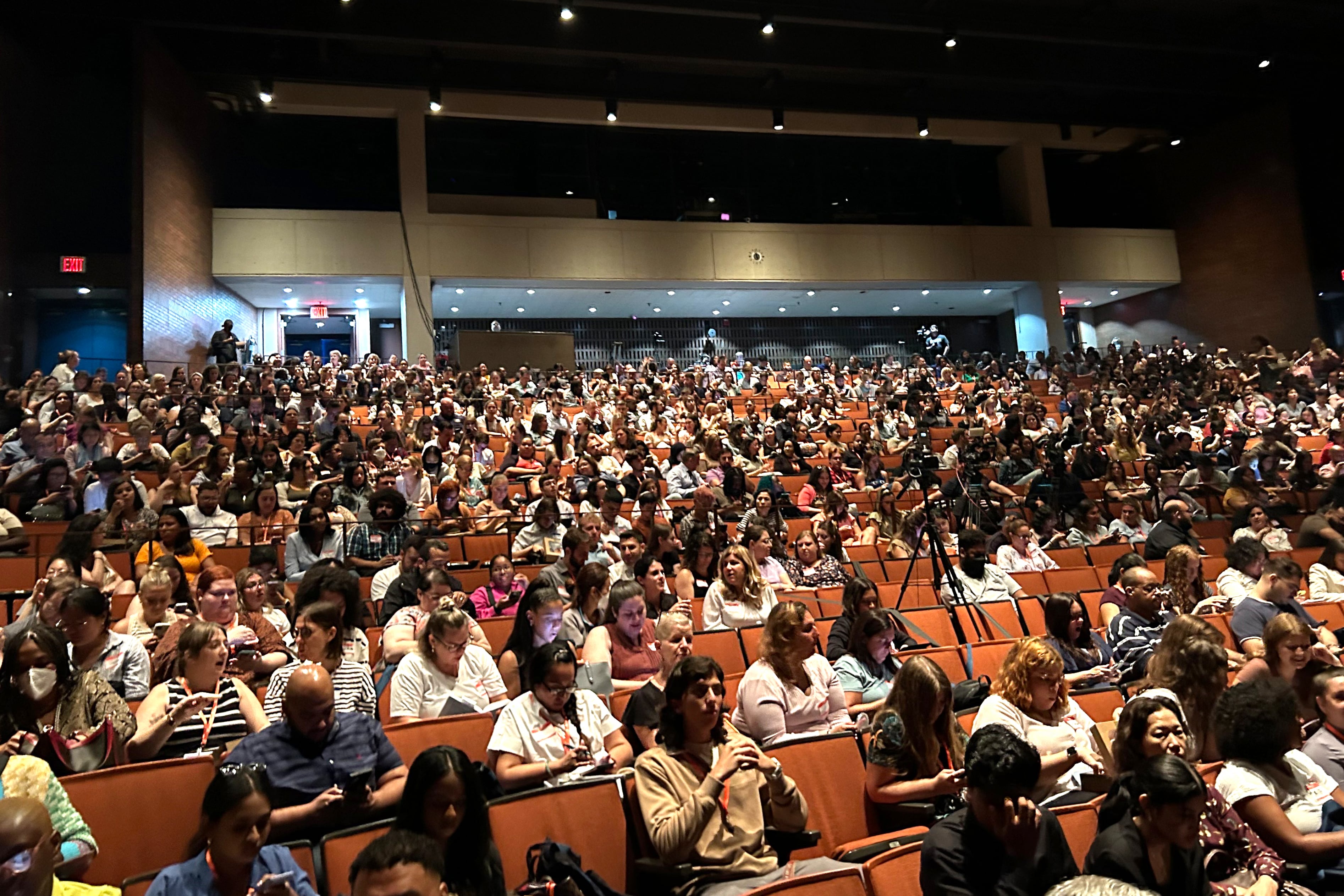 Teachers sit in a large auditorium.