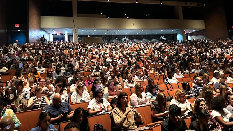 Teachers sit in a large auditorium.