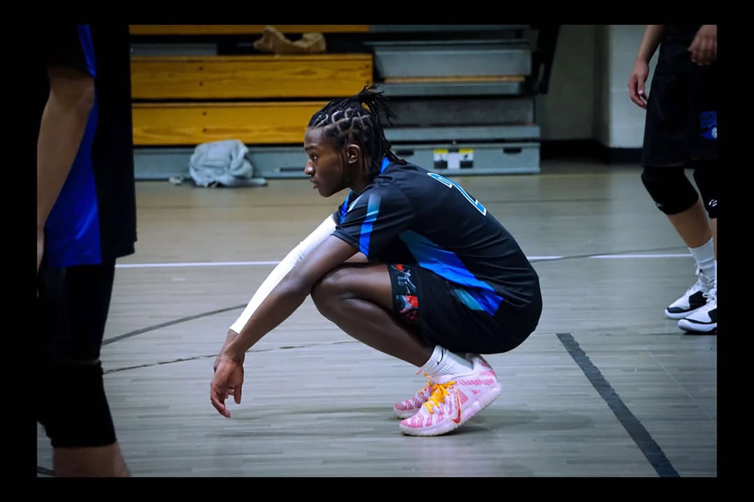 A photograph of a Black high school athlete crouching over during a volleyball game.