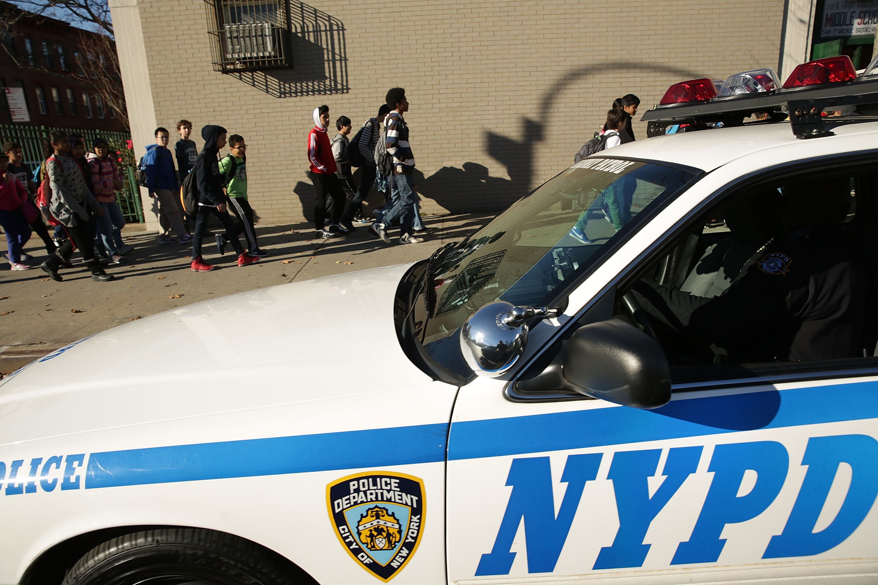 A New York Police Department cruiser sits in the foreground as students walk past on the sidewalk.