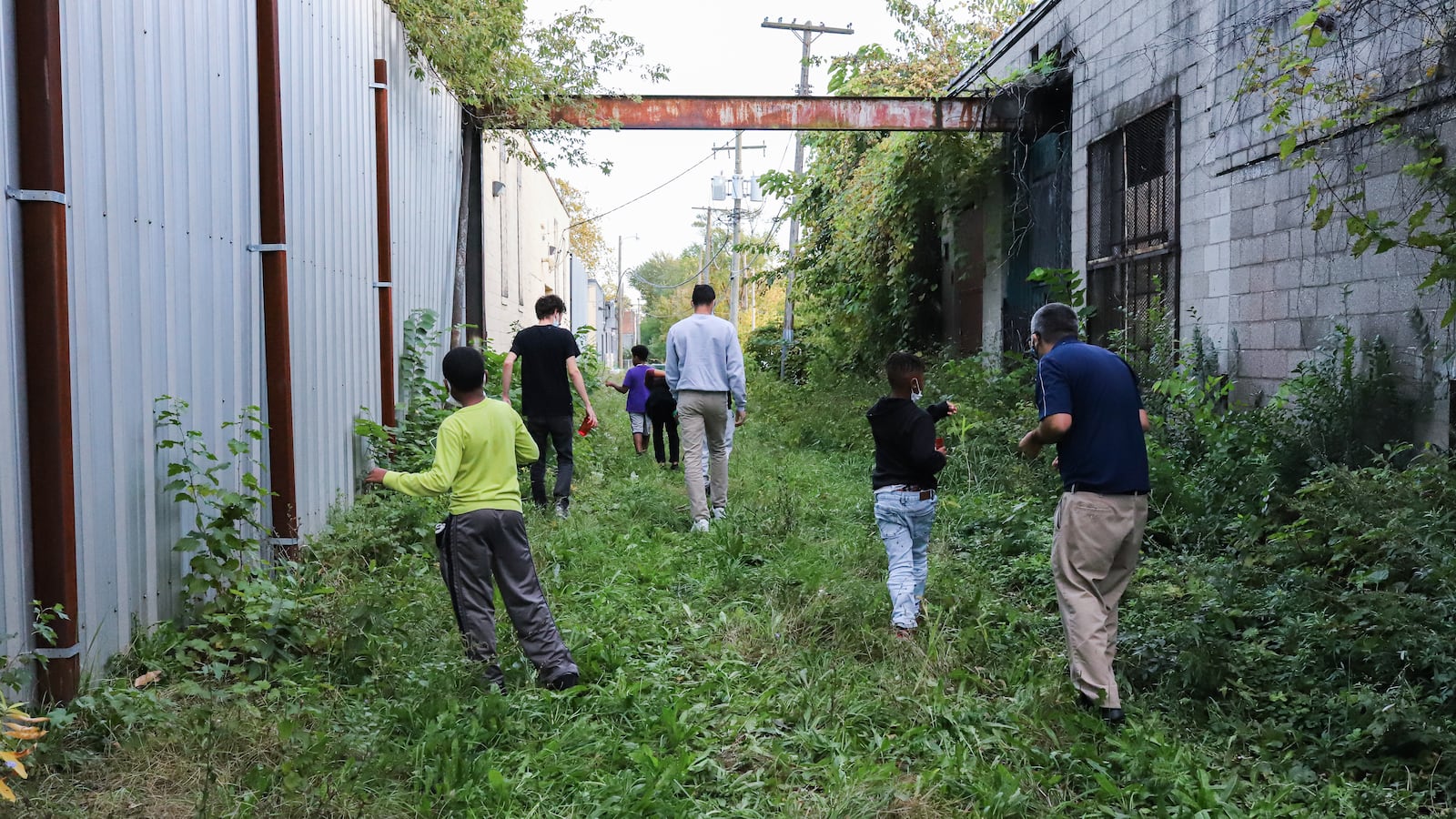 Students and teachers walk down a green patch between two industrial buildings off-set from one another.