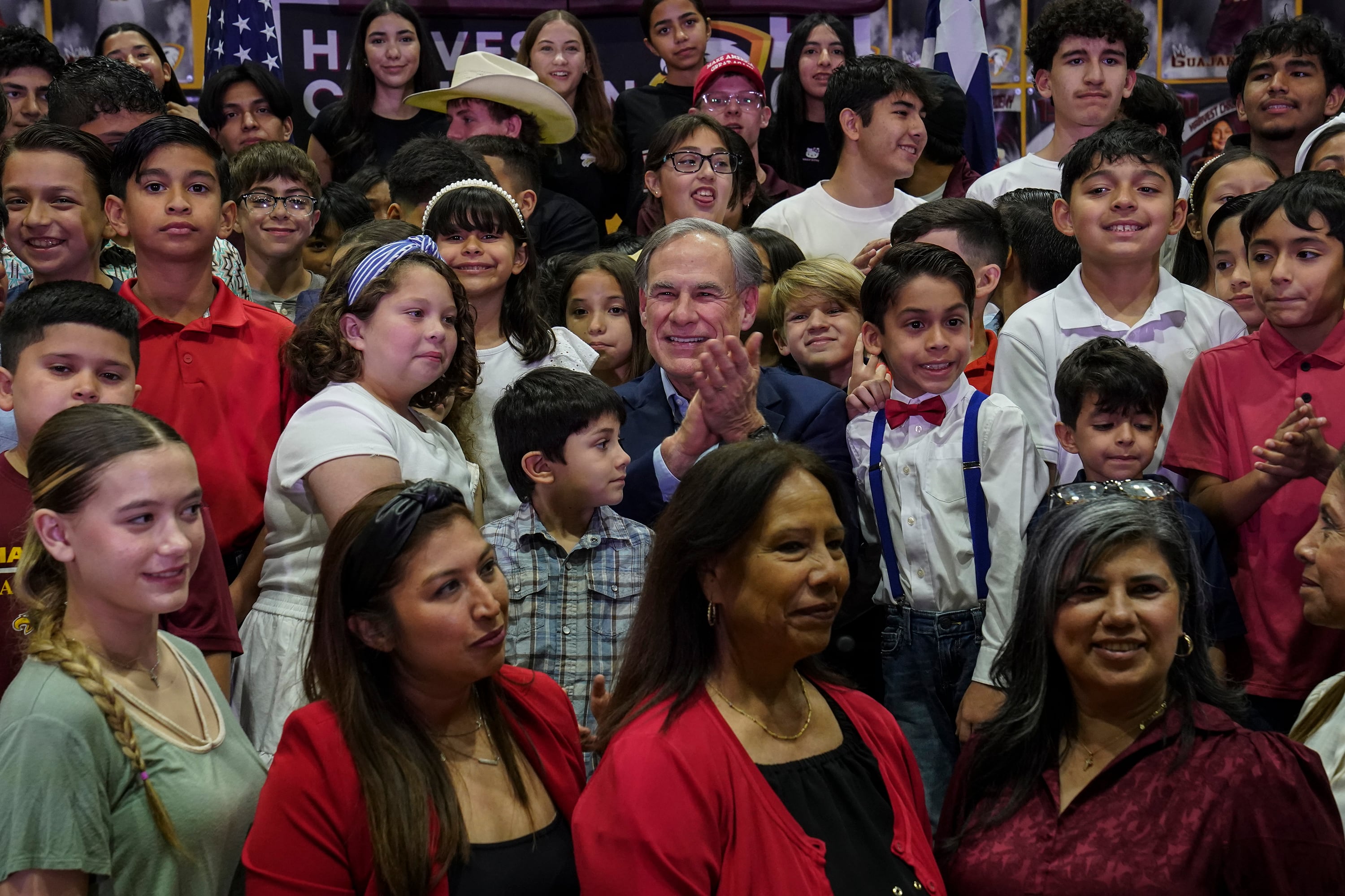 A man in a dark suit jacket applauds surrounded by a crowd