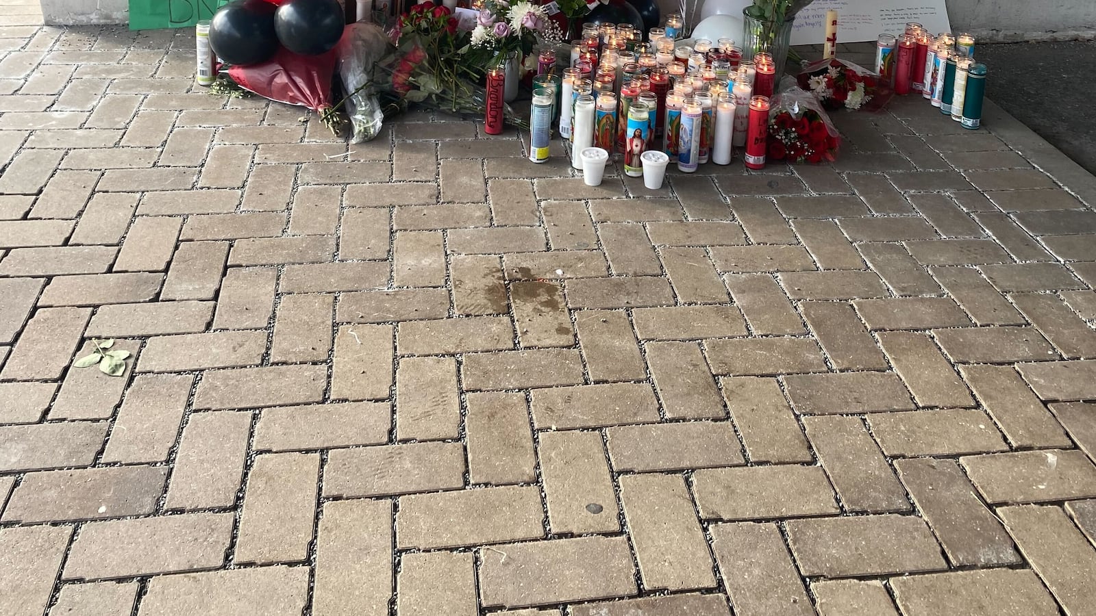 Signs mentioning Brandon Perez and Nathan Billegas hang on the wall. On the ground, there are balloons, candles, and flowers for a memorial to the two students at Benito Juarez High School in Chicago.