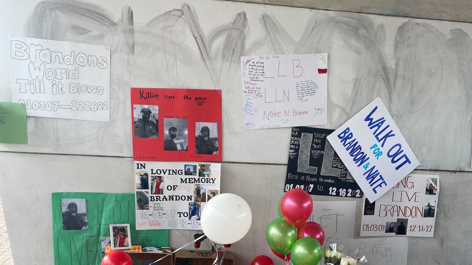Signs mentioning Brandon Perez and Nathan Billegas hang on the wall. On the ground, there are balloons, candles, and flowers for a memorial to the two students at Benito Juarez High School in Chicago.