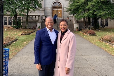 A Black man and woman stand next to each other posing for a portrait outside of a large stone school building.