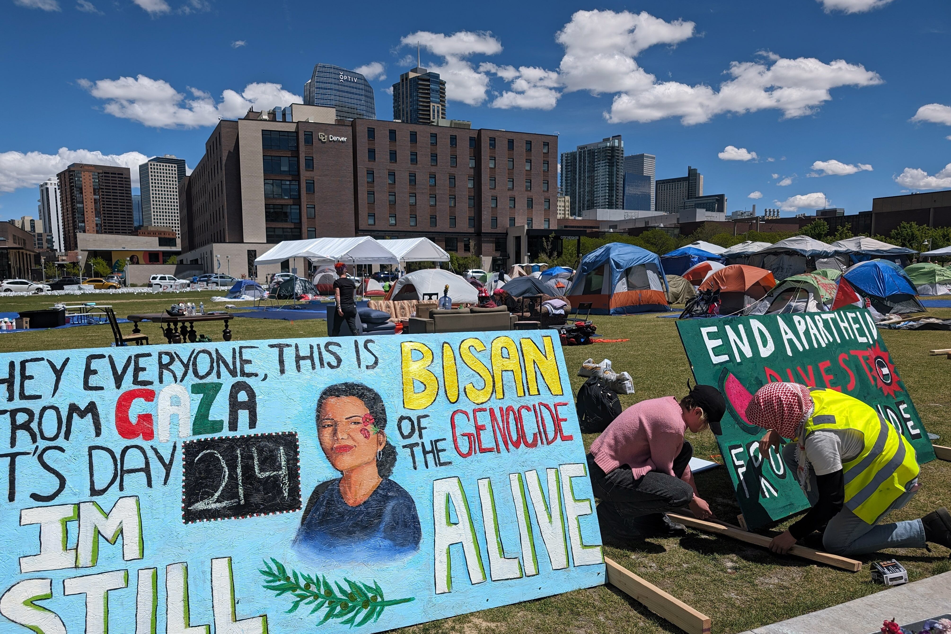 A large hand painted sign with a portrait of Bisan sits on a green lawn with students and buildings in the background.
