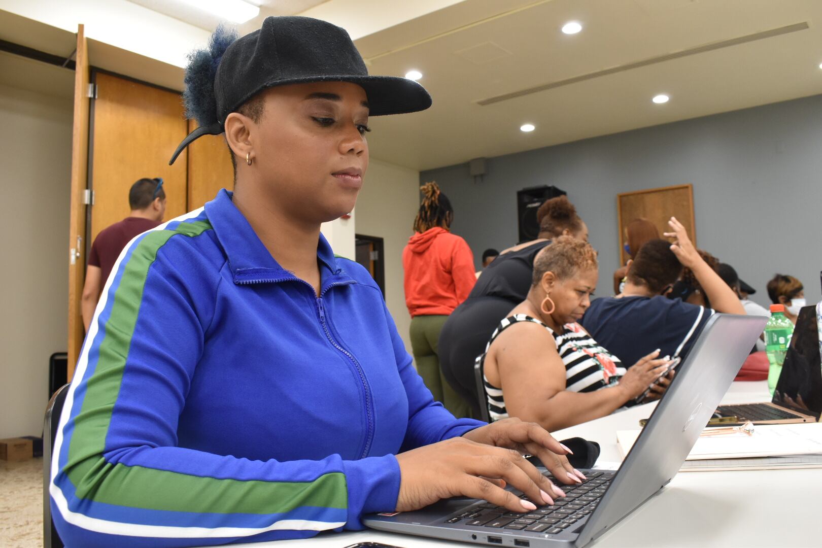 A woman wearing a blue and green jacket types on a silver laptop.