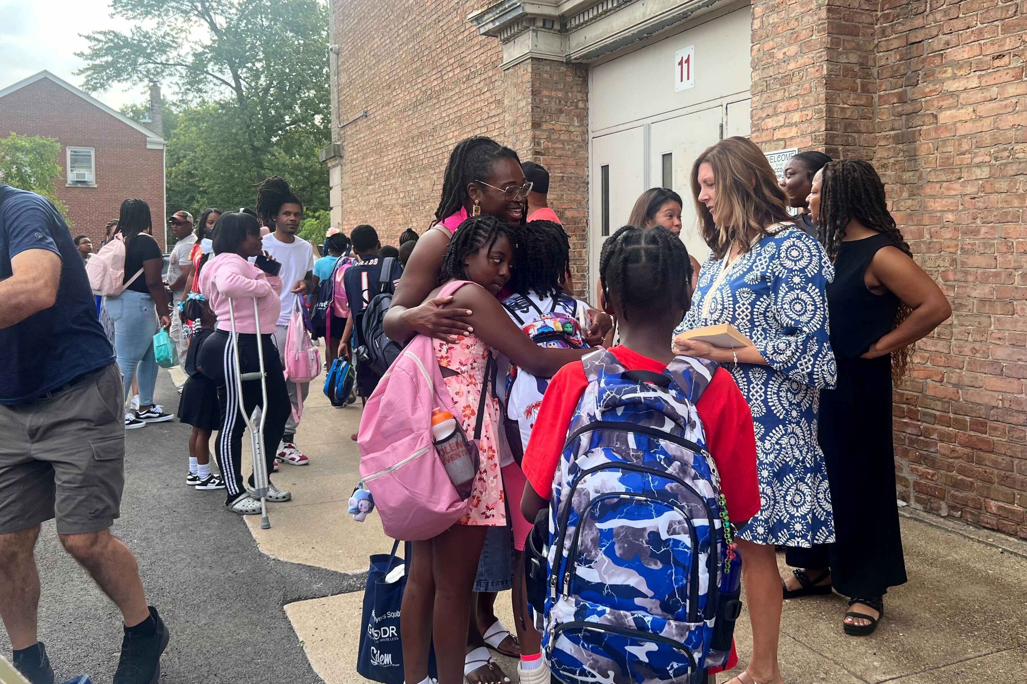 A group of adults and students outside of a school building on the first day of school.
