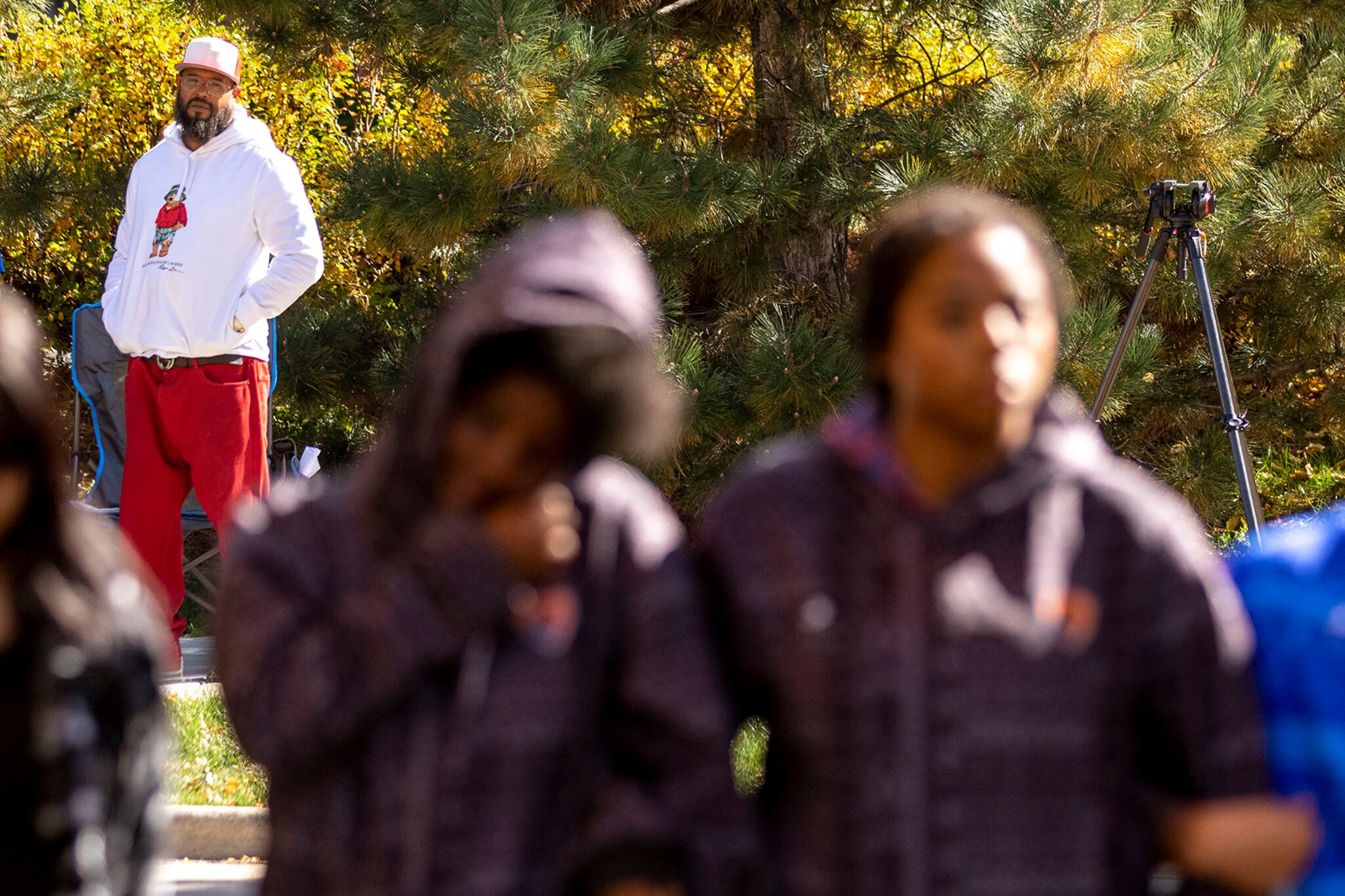 A man wearing red pants and a white sweatshirt stands with his hands in his sweatshirt pocket.