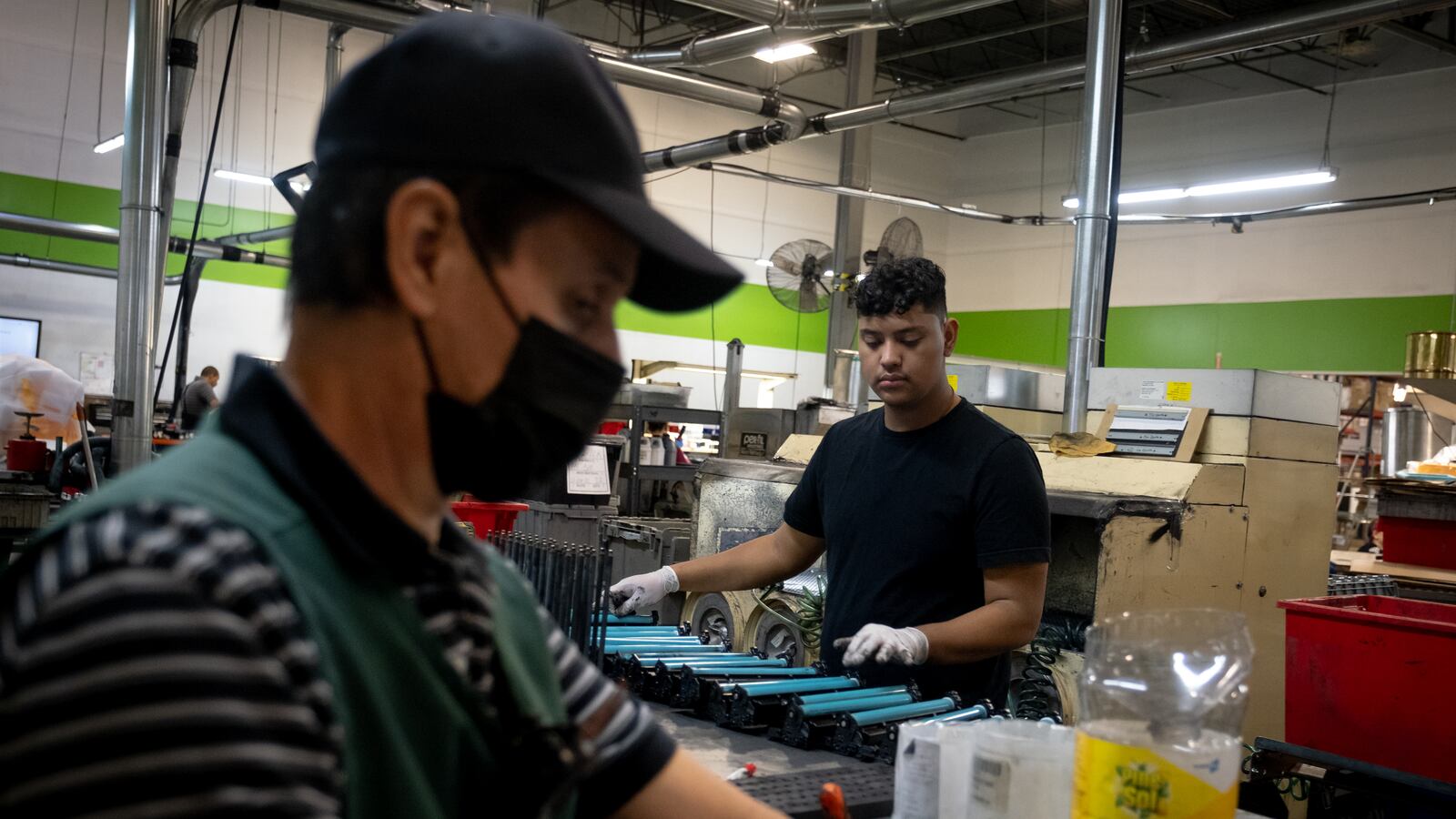 Two men, one young and one older, work at their station in an ink cartridge factory.