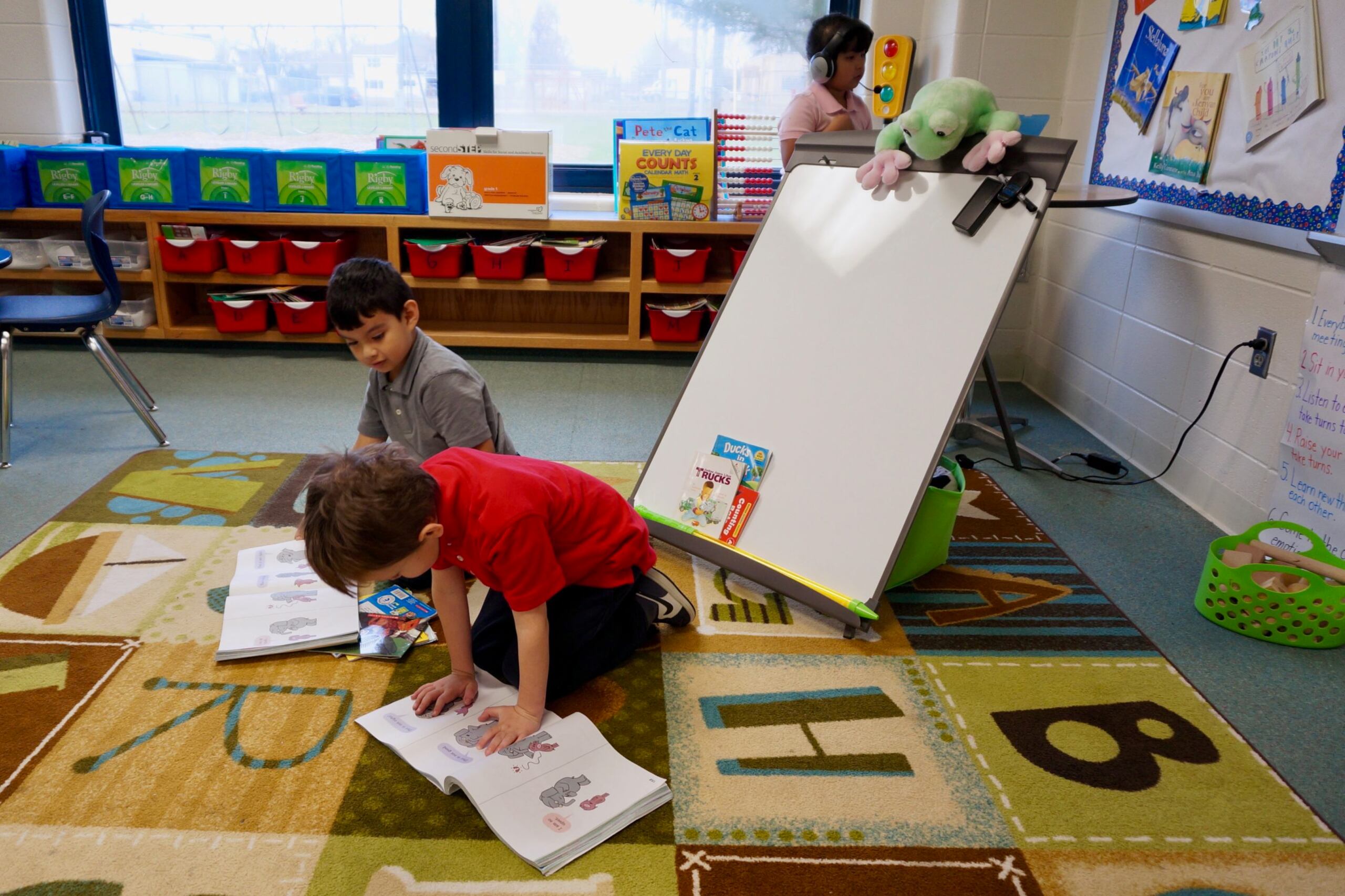 Two children read picture books in a classroom.