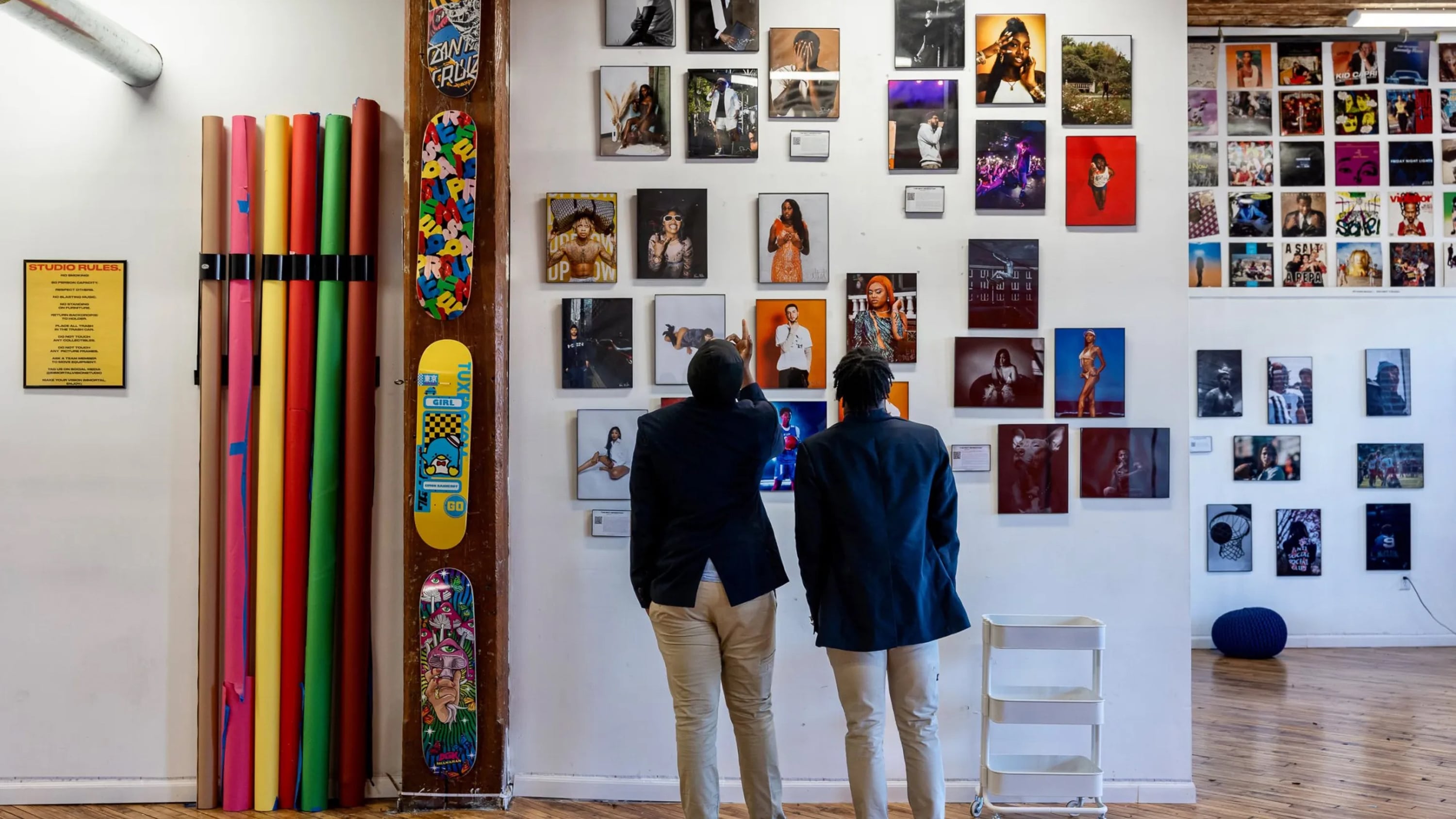Two boys look up at photographs and skateboards hanging on a white wall.