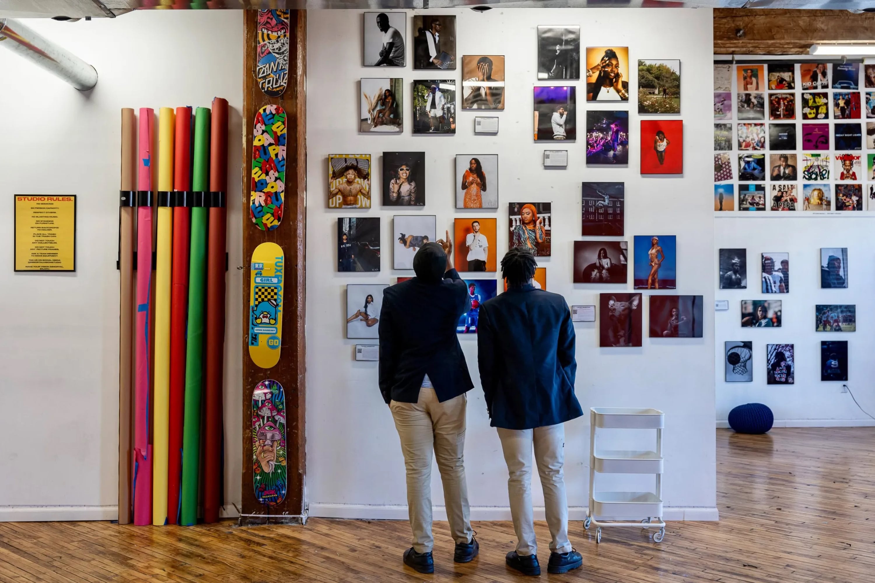 Two boys look up at photographs and skateboards hanging on a white wall.