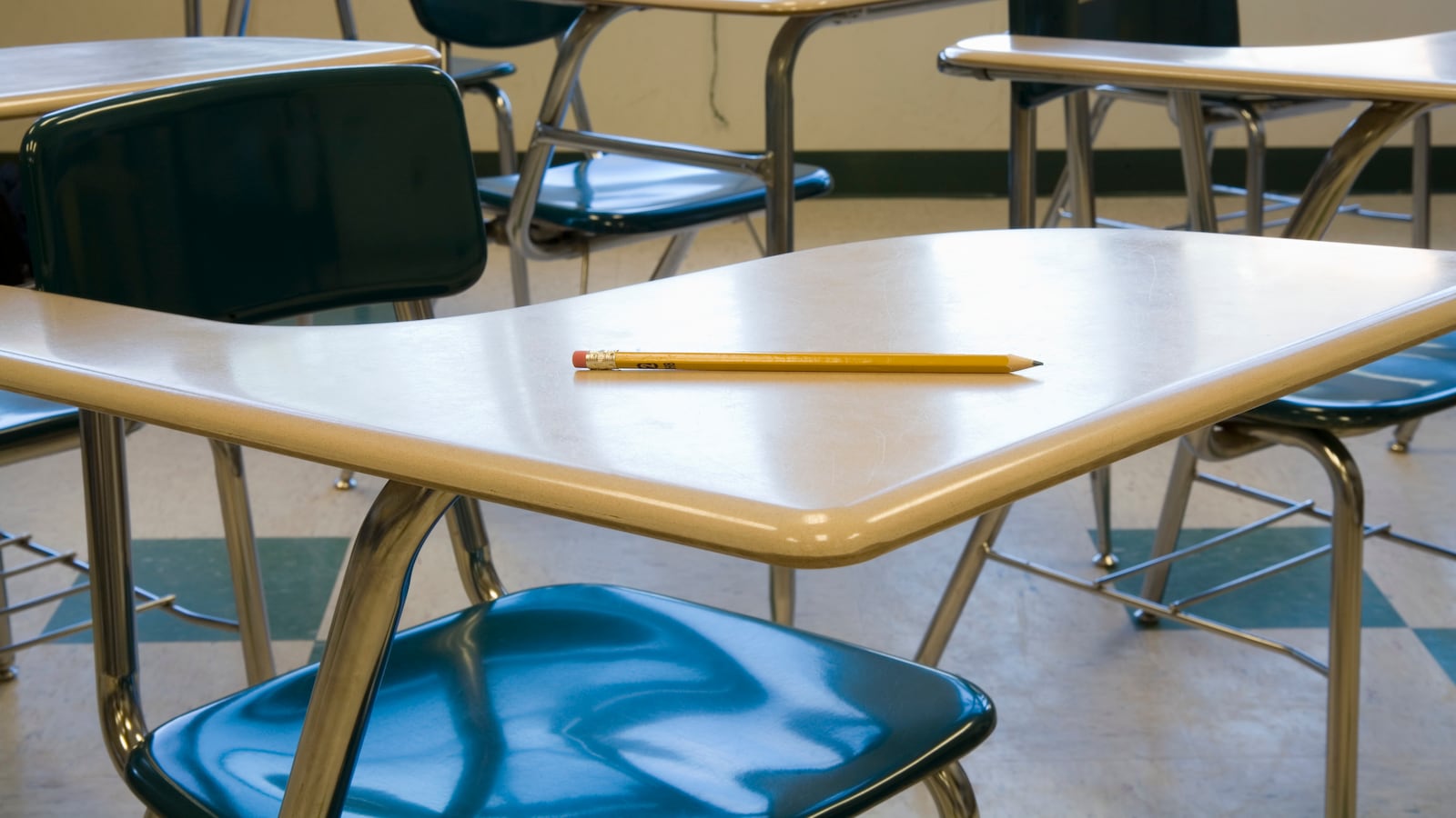A pencil on a wooden school desk in an empty classroom.