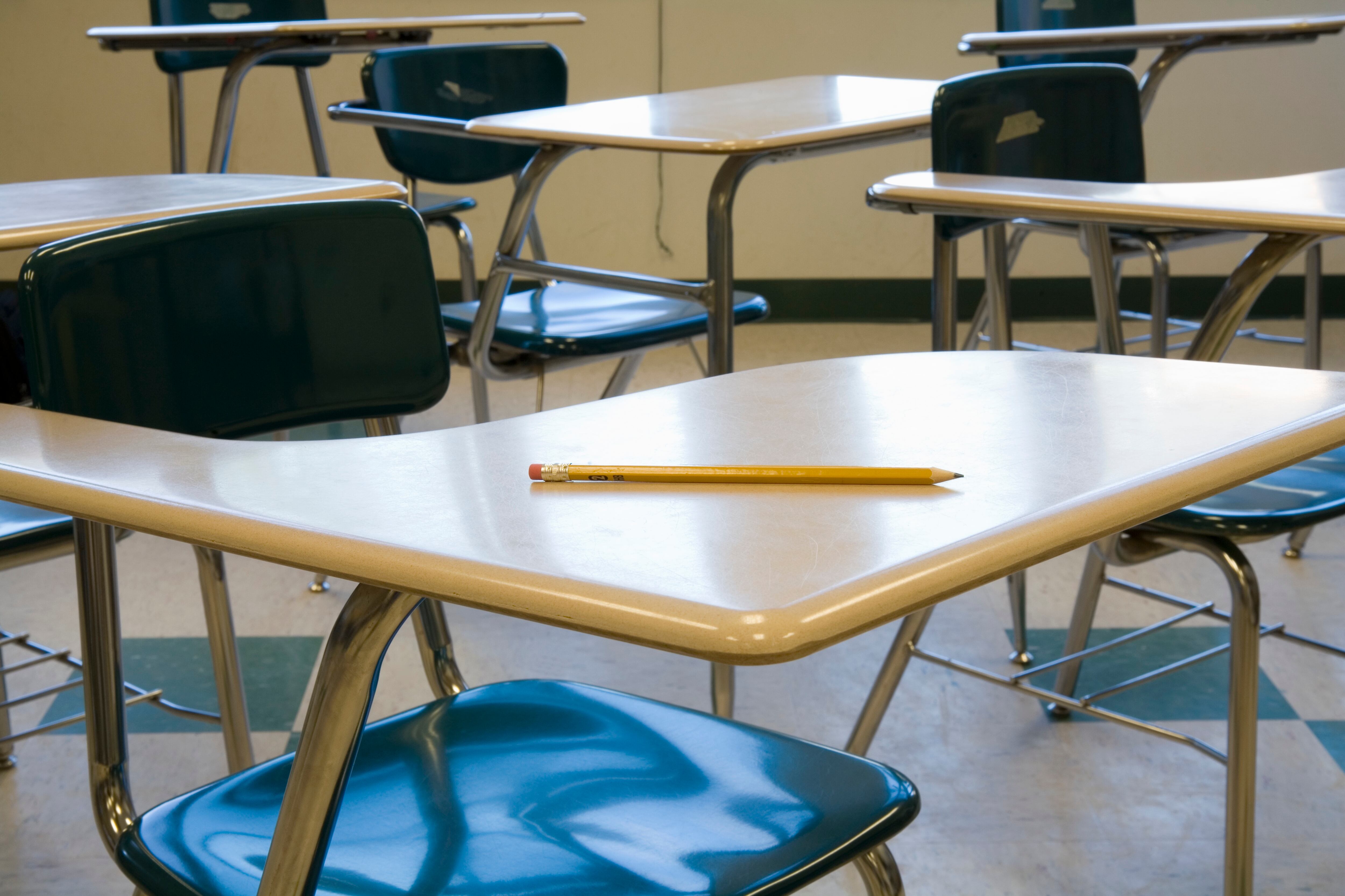 A pencil on a wooden school desk in an empty classroom.