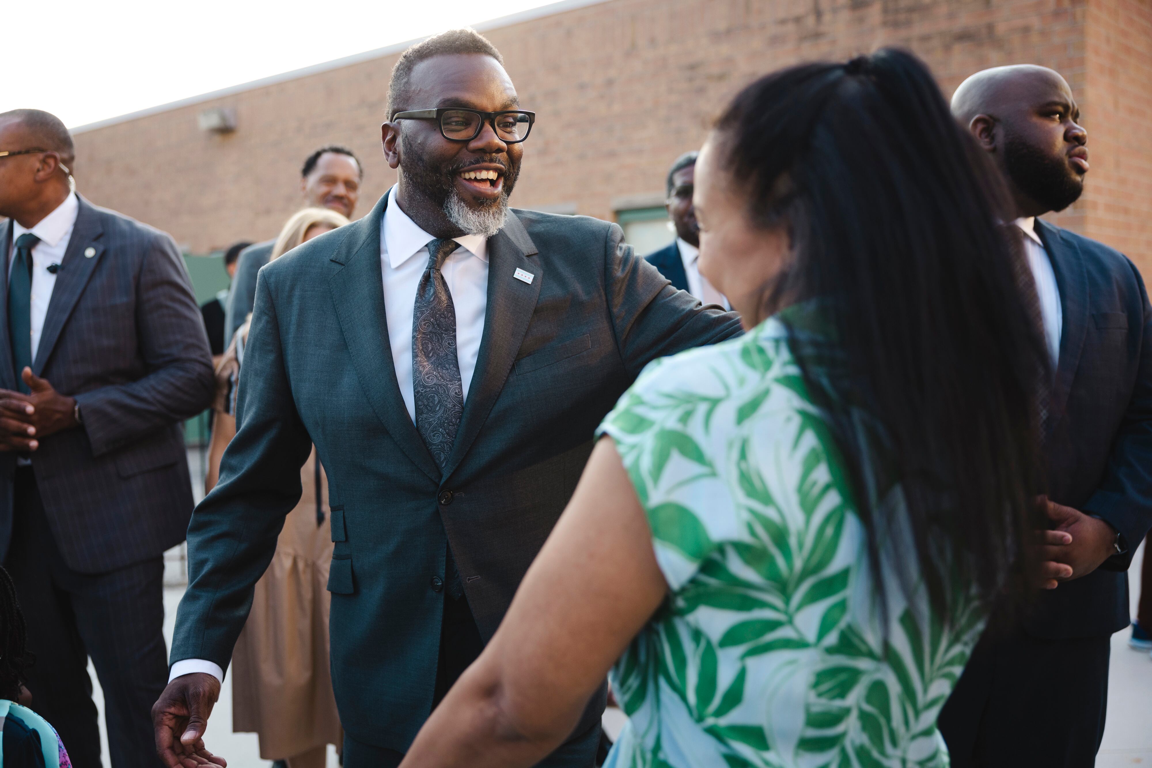 A man in a suit stands next to other adults and students outside.