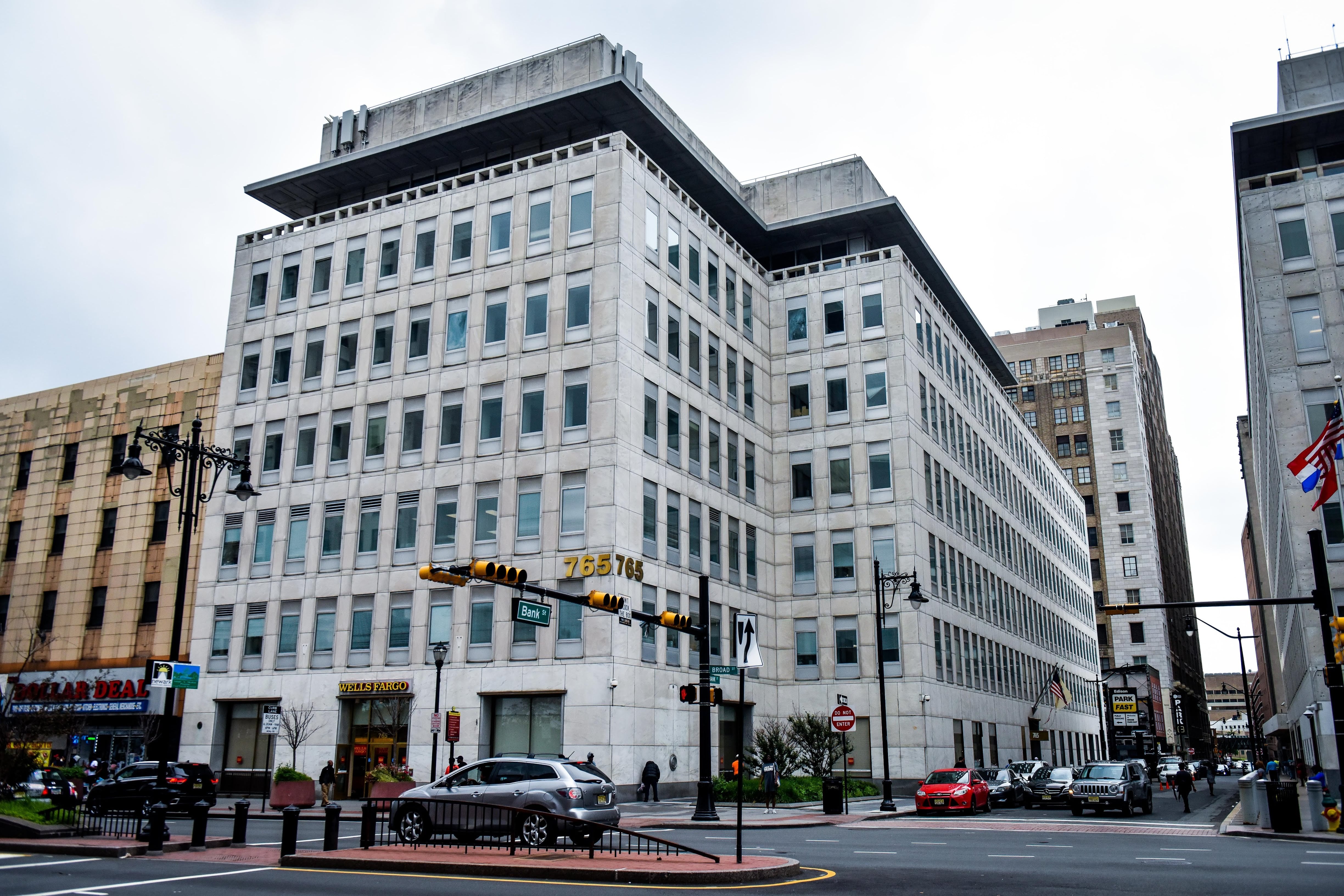 Cars drive by a white building on the corner of Broad Street in Newark