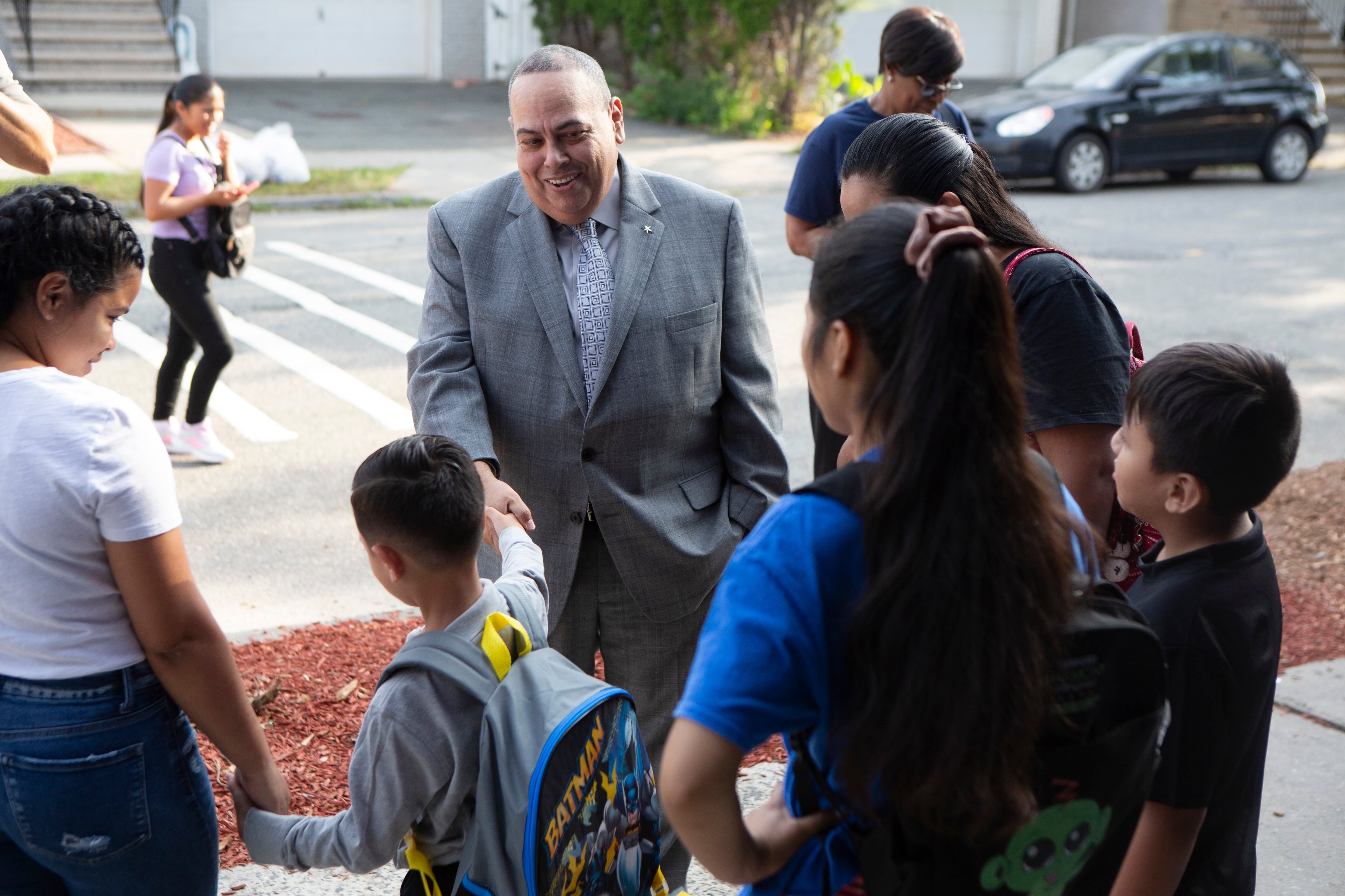 A photograph of a man in a suit talking with students and guardians outside.