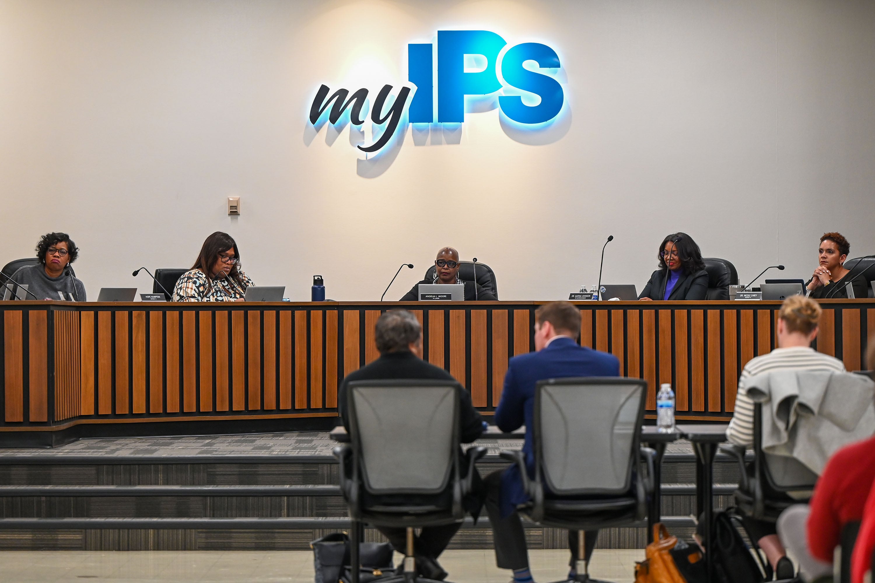 A group of people sit in a row in the front of a large conference room.