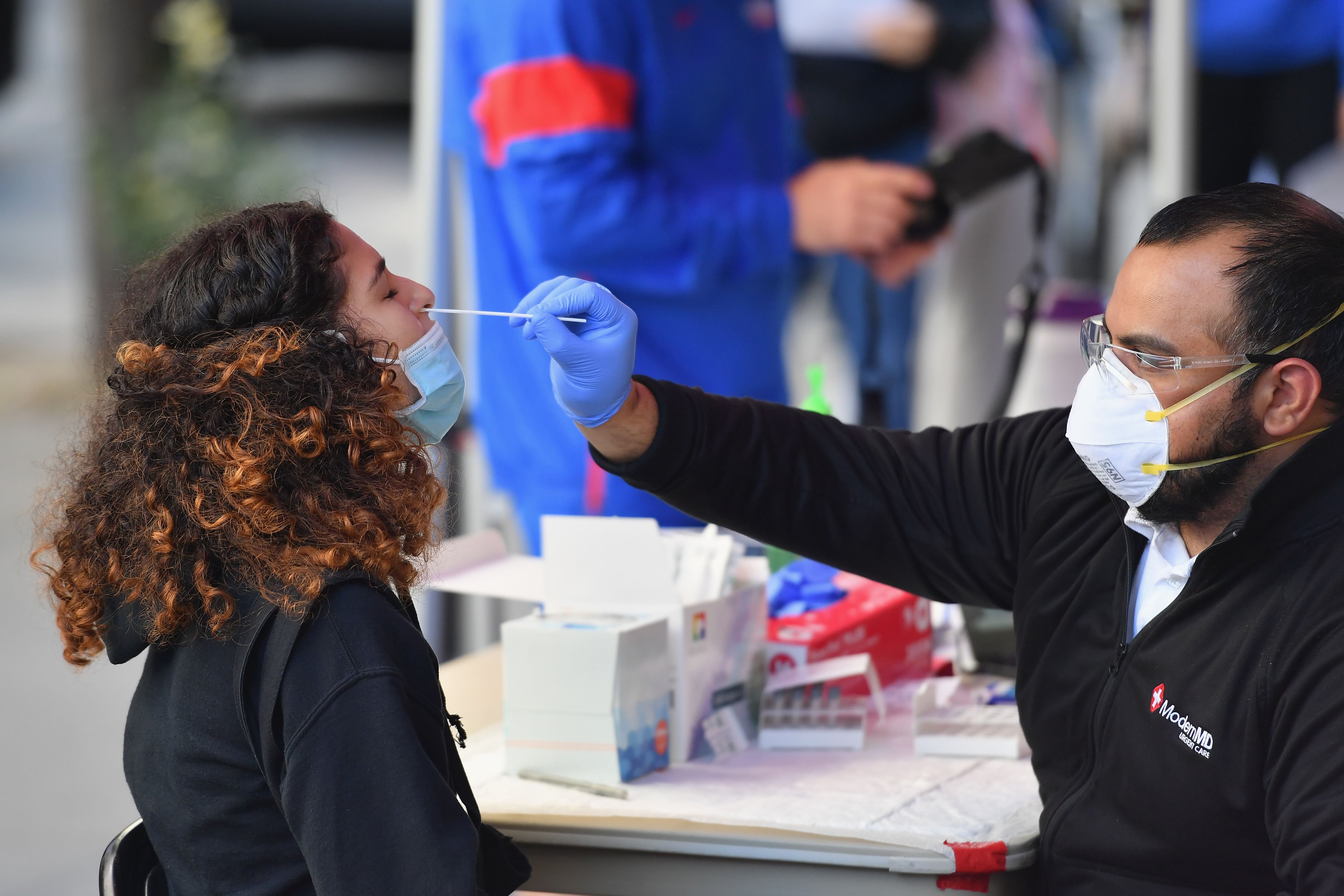 A student wearing a blue face mask is tested for COVID by a medical professional via nasal swab.